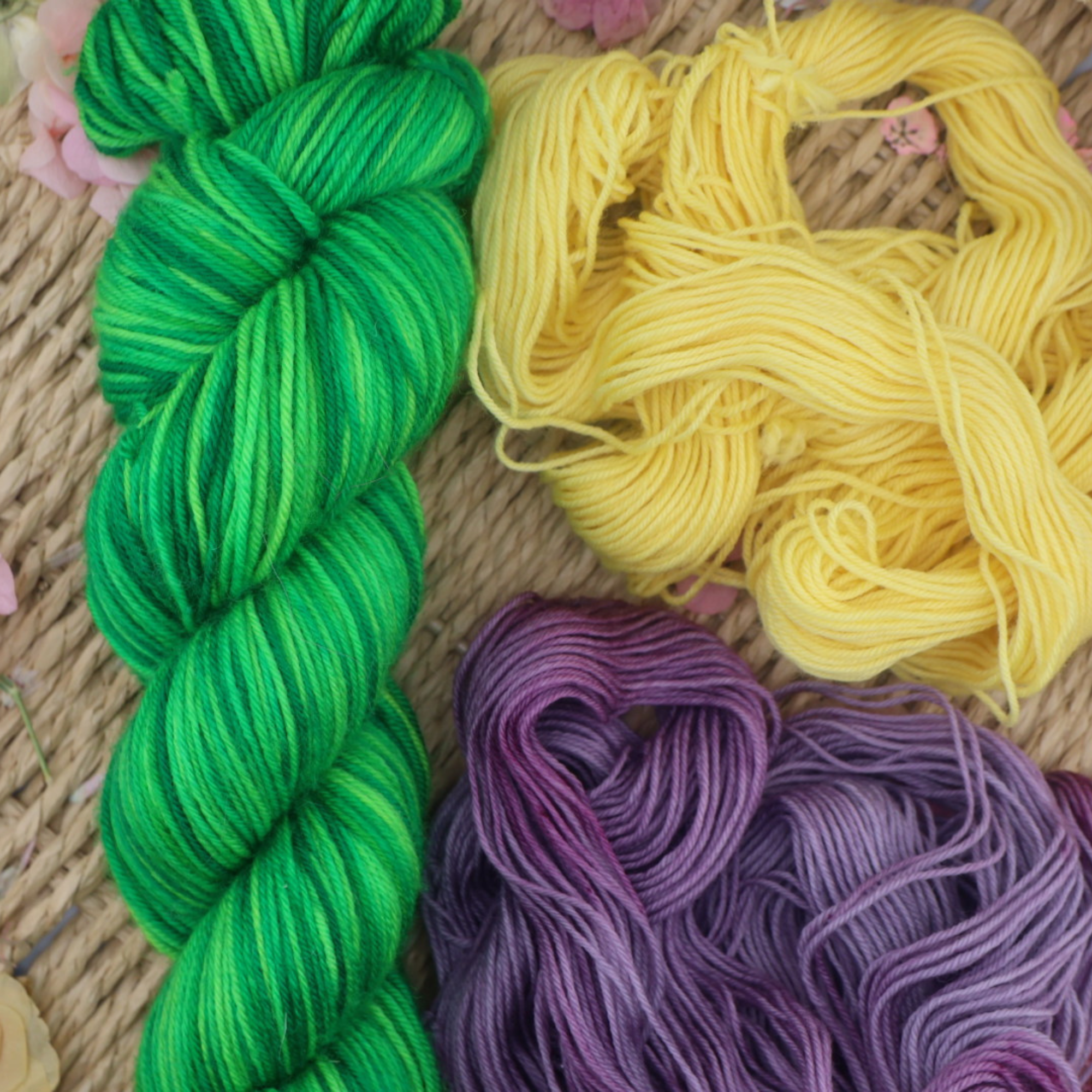 Loose strands of green, yellow and purple yarn arranged on a woven surface, showing colour blending and fibre detail.