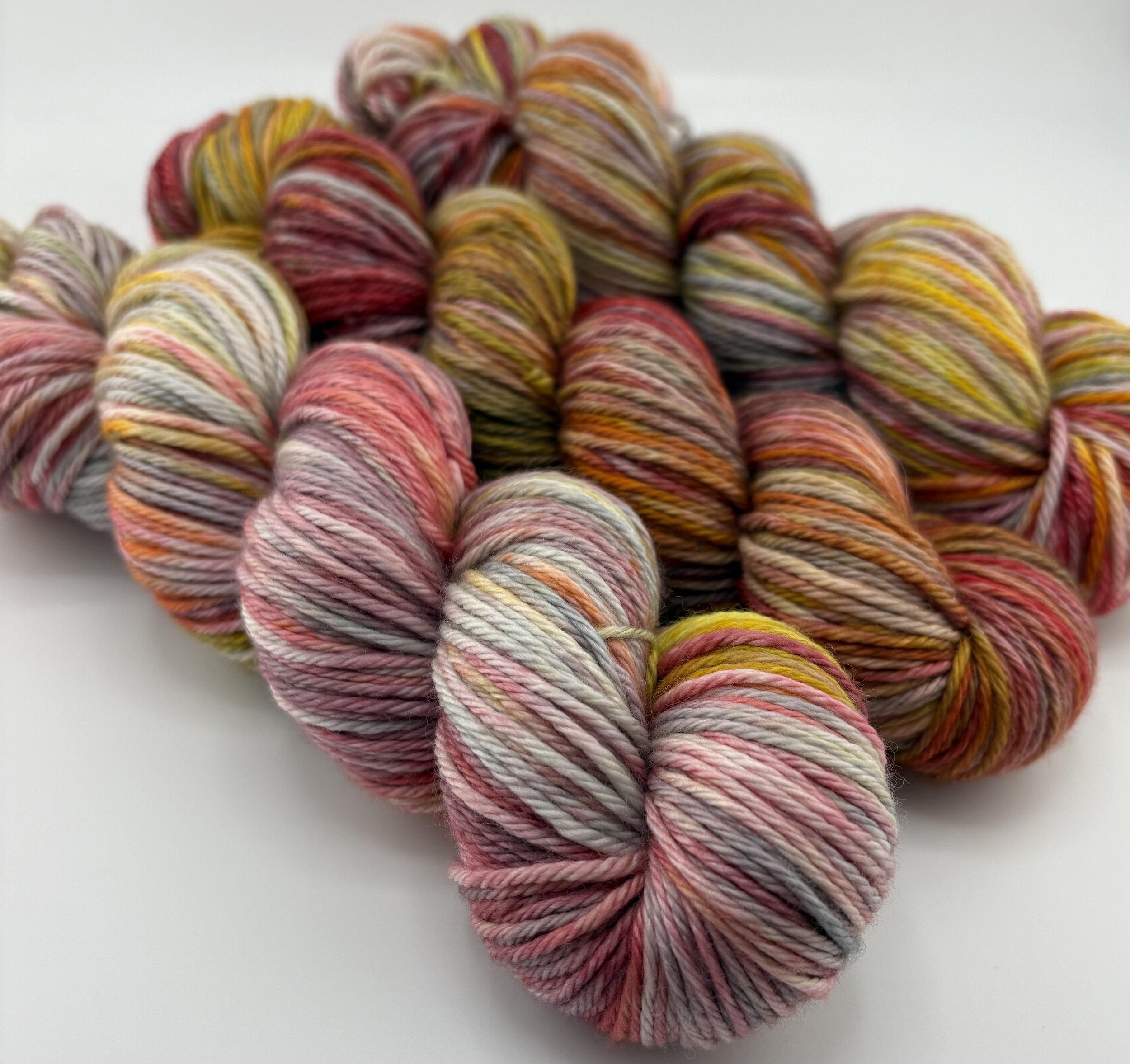 Hand‑dyed yarn skeins in red, pink, yellow, orange and grey variegated shades arranged together