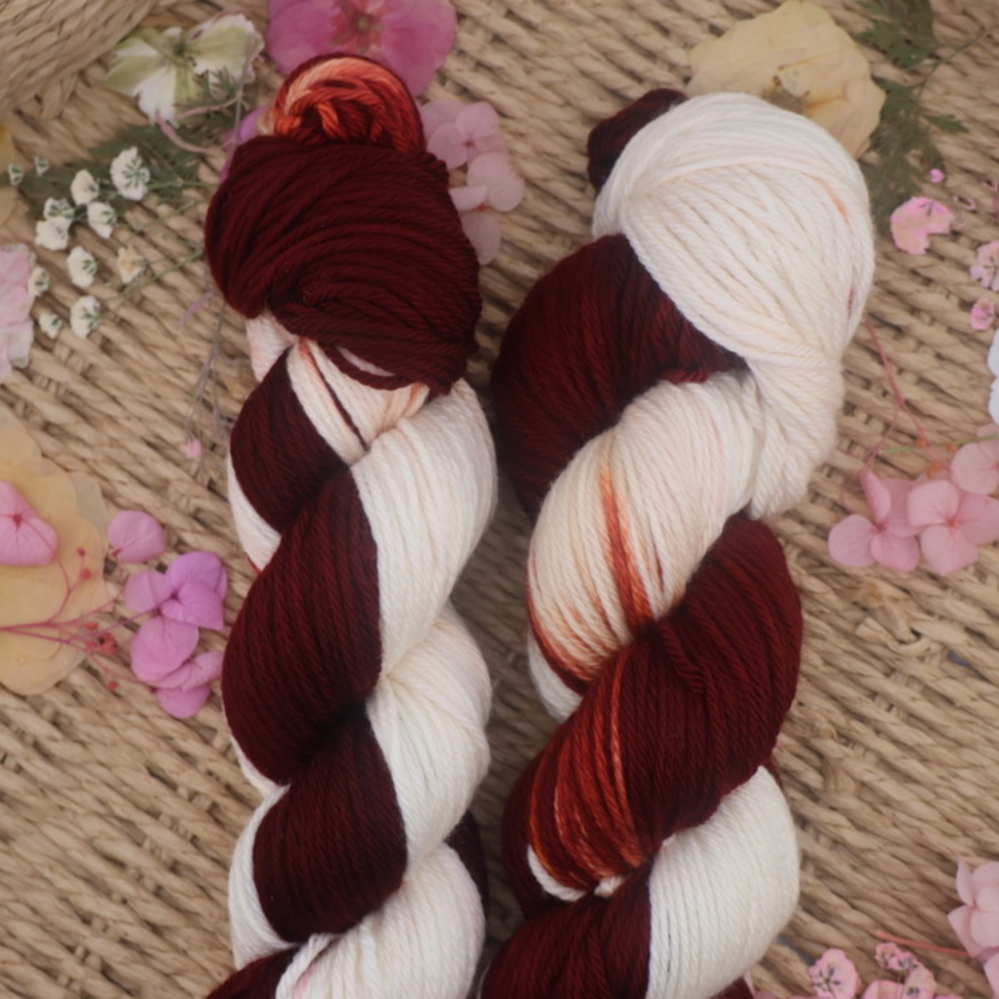 Close‑up of two burgundy and cream hand‑dyed yarn skeins in a woven basket, showing soft fibre texture and subtle colour transitions