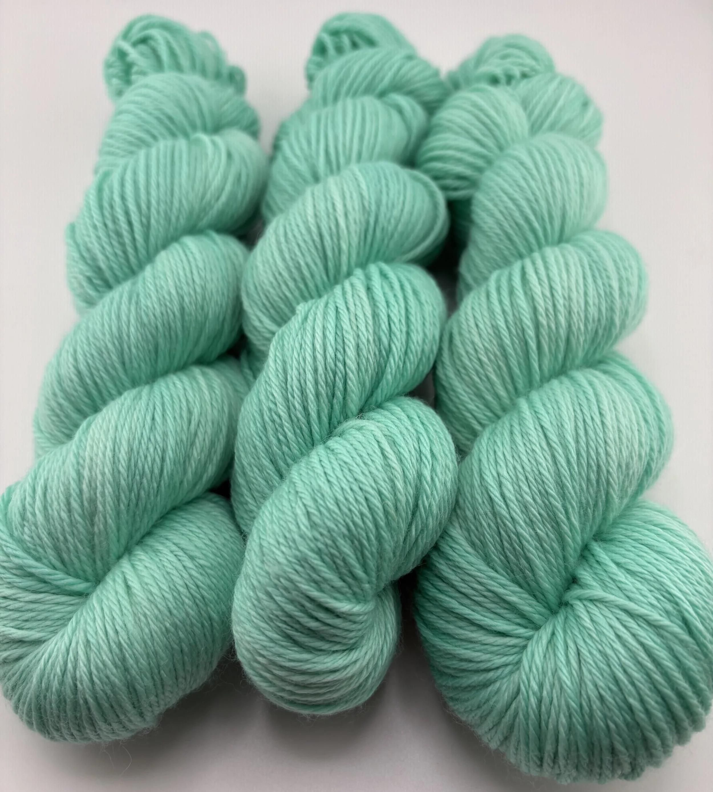 Three Hand‑dyed yarn skeins in mint green shades arranged in a neat pile.