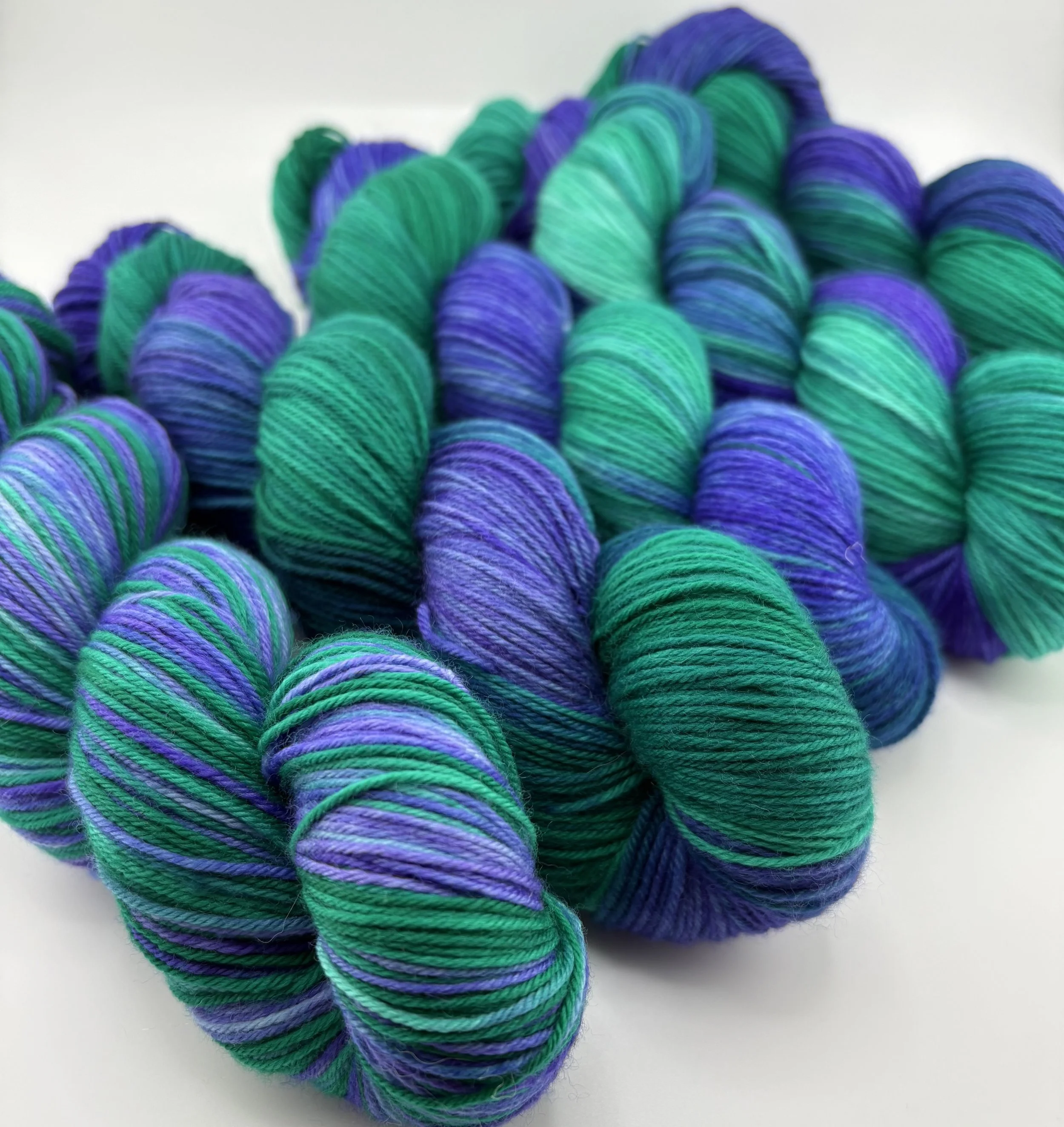 Multiple skeins of multicolored yarn in shades of purple, green, and teal.