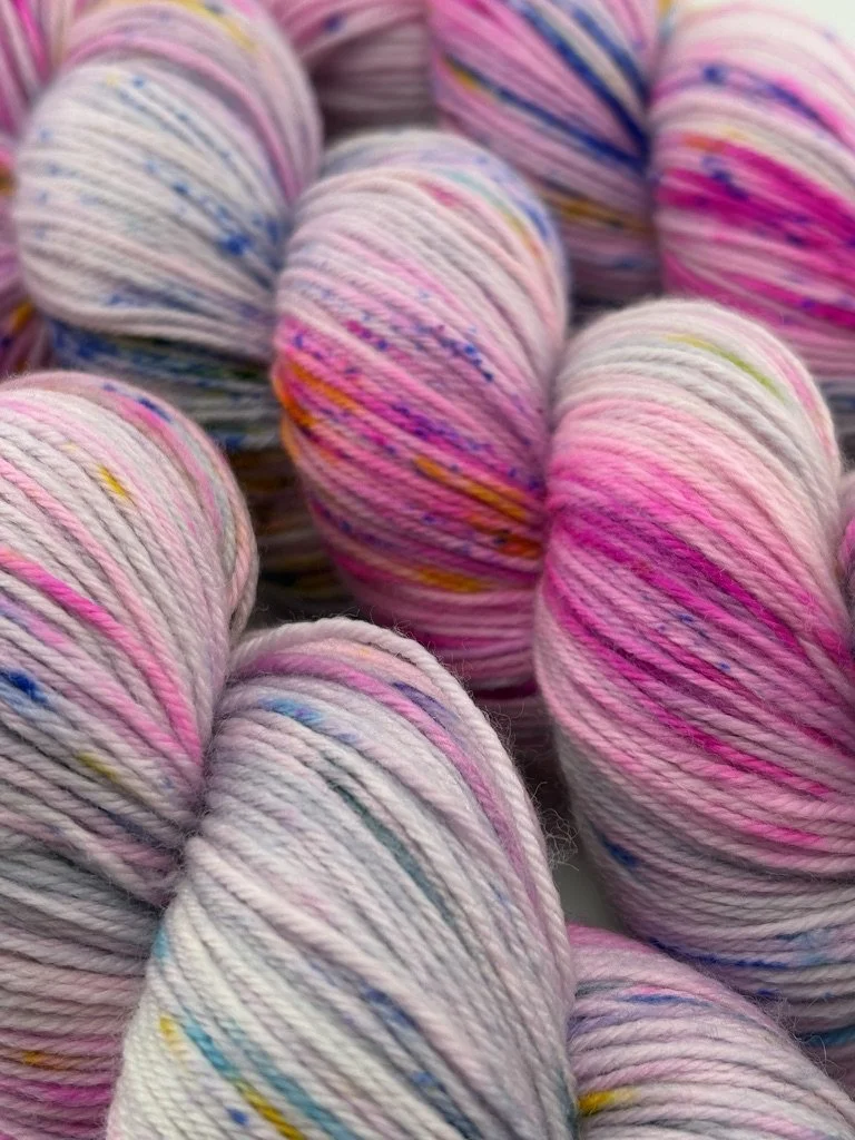 Soft pink skeins featuring blue, yellow, orange, and magenta speckles, displayed side by side