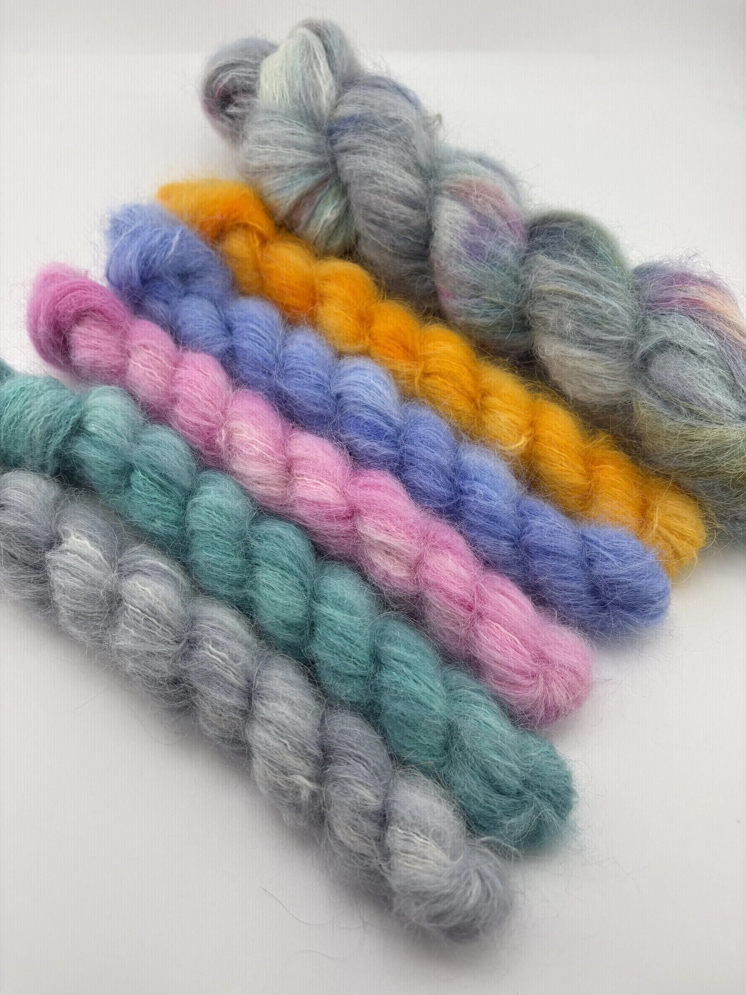 Multiple colorful skeins of soft, fluffy yarn in pastel and bright shades arranged on a white surface.