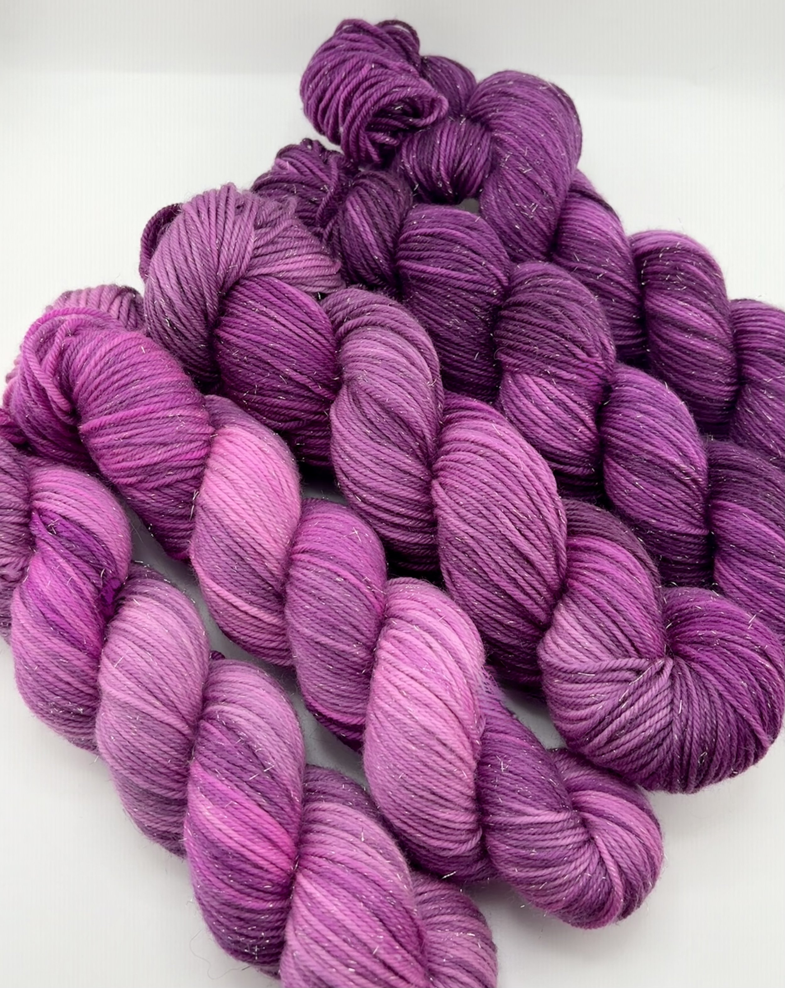 Multiple skeins of purple and pink variegated yarn arranged on a white surface.