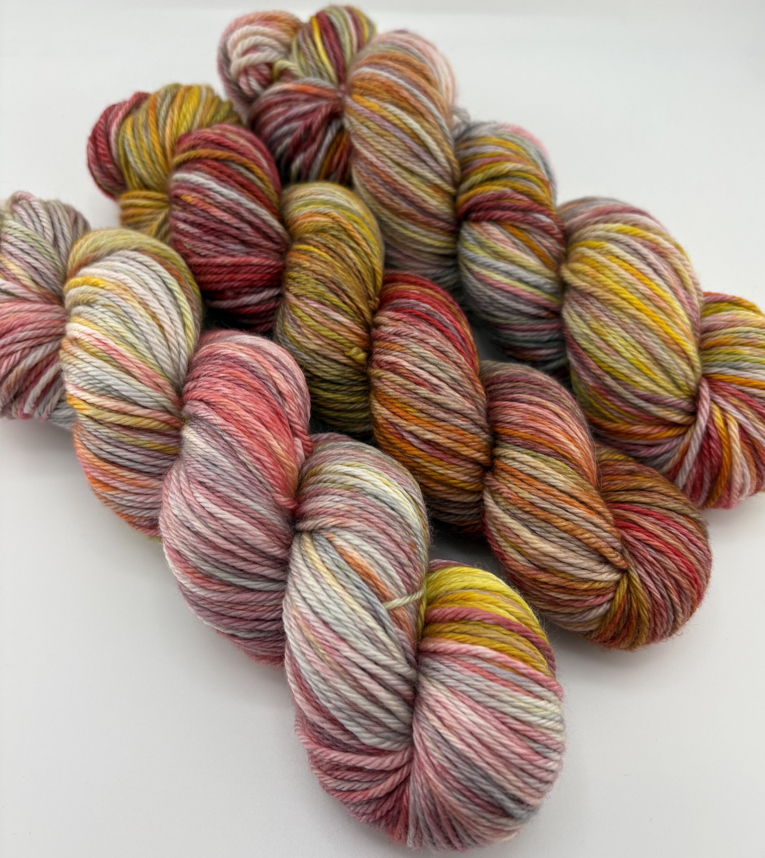 Hand‑dyed yarn skeins in red, pink, yellow, orange and grey variegated shades arranged together