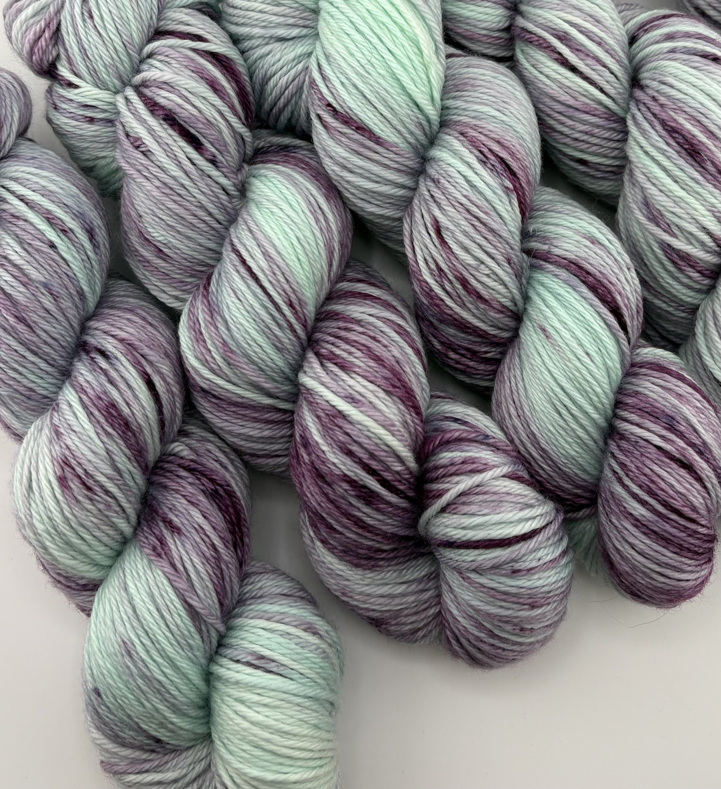 Hand‑dyed yarn skeins in mint green and deep purple variegated shades arranged together