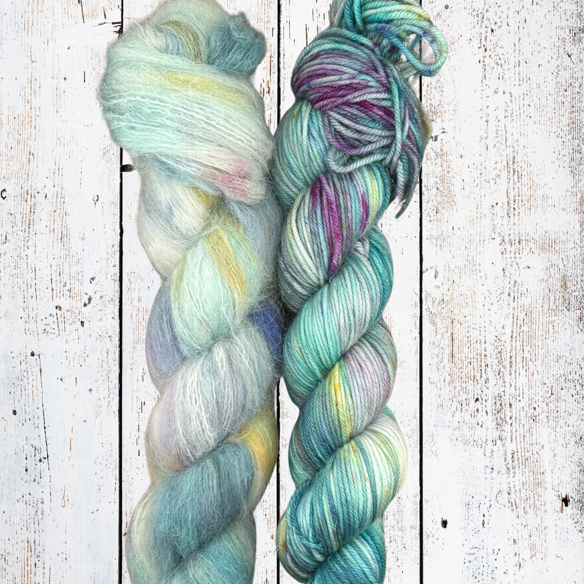Two skeins of teal and sea‑green hand‑dyed yarn on a white wooden background, showing smooth twist and colour blend.