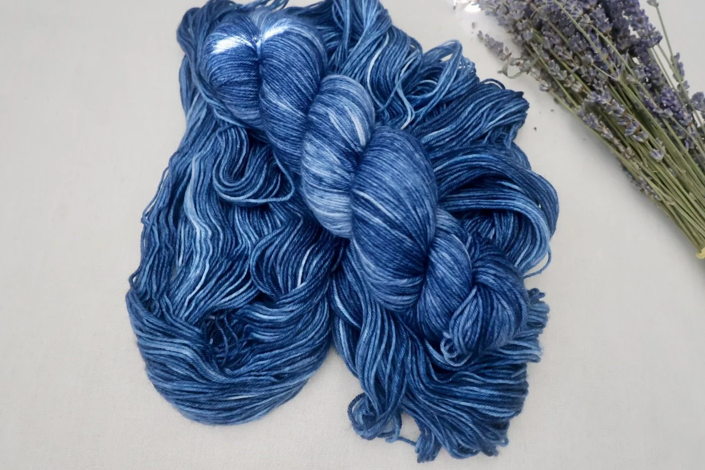Four skeins of blue merino nylon yarn featuring ocean‑inspired tonal shifts, photographed with dried lavender.