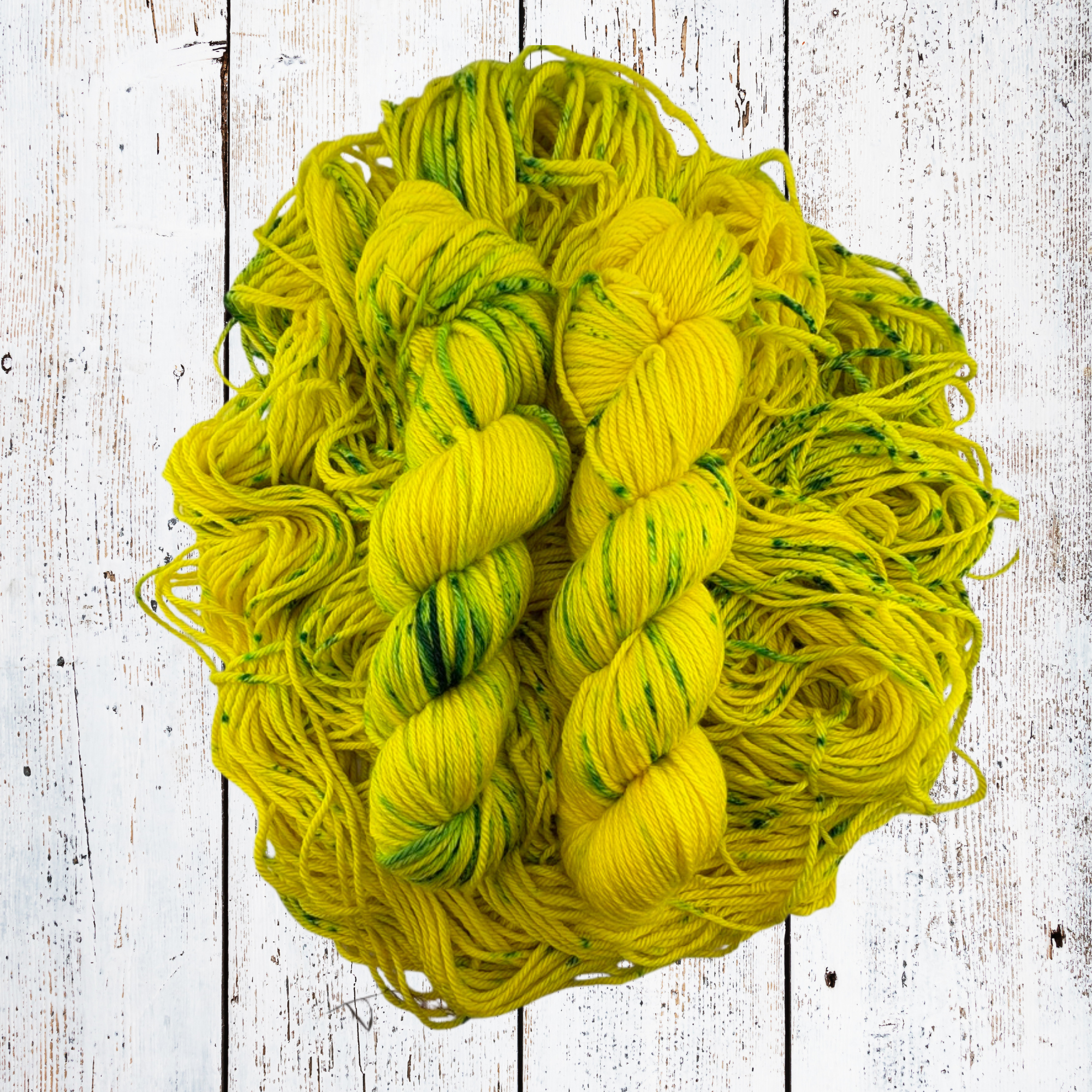Yellow‑green merino yarn skeins resting on a bed of loose, untwisted fibres on a white wooden surface, emphasising colour depth and softness