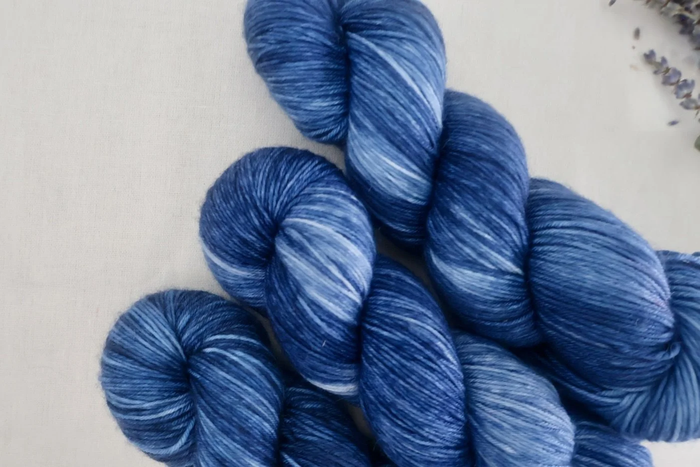 Variegated blue hand‑dyed yarn with deep indigo and soft sky‑blue tones, styled beside lavender sprigs.