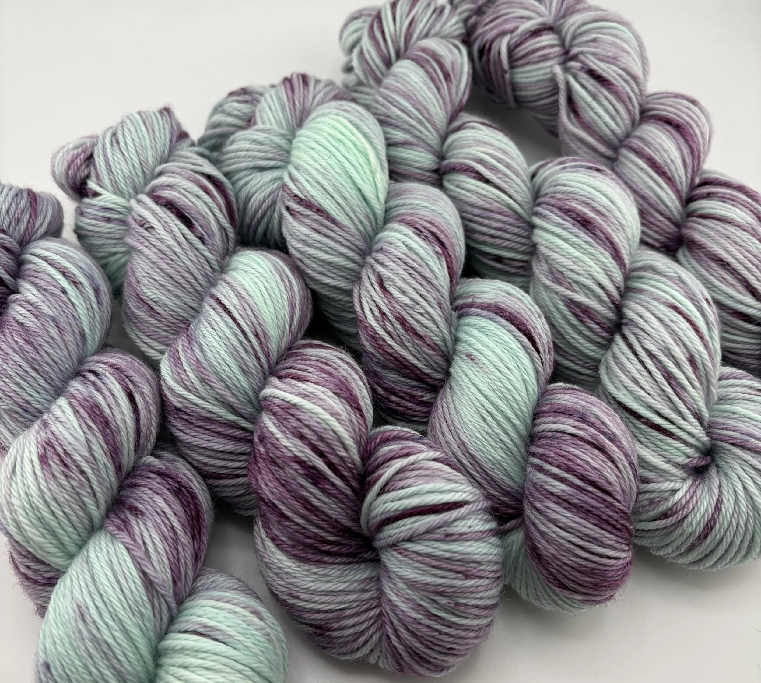 Hand‑dyed yarn skeins in mint green and deep purple variegated shades arranged together