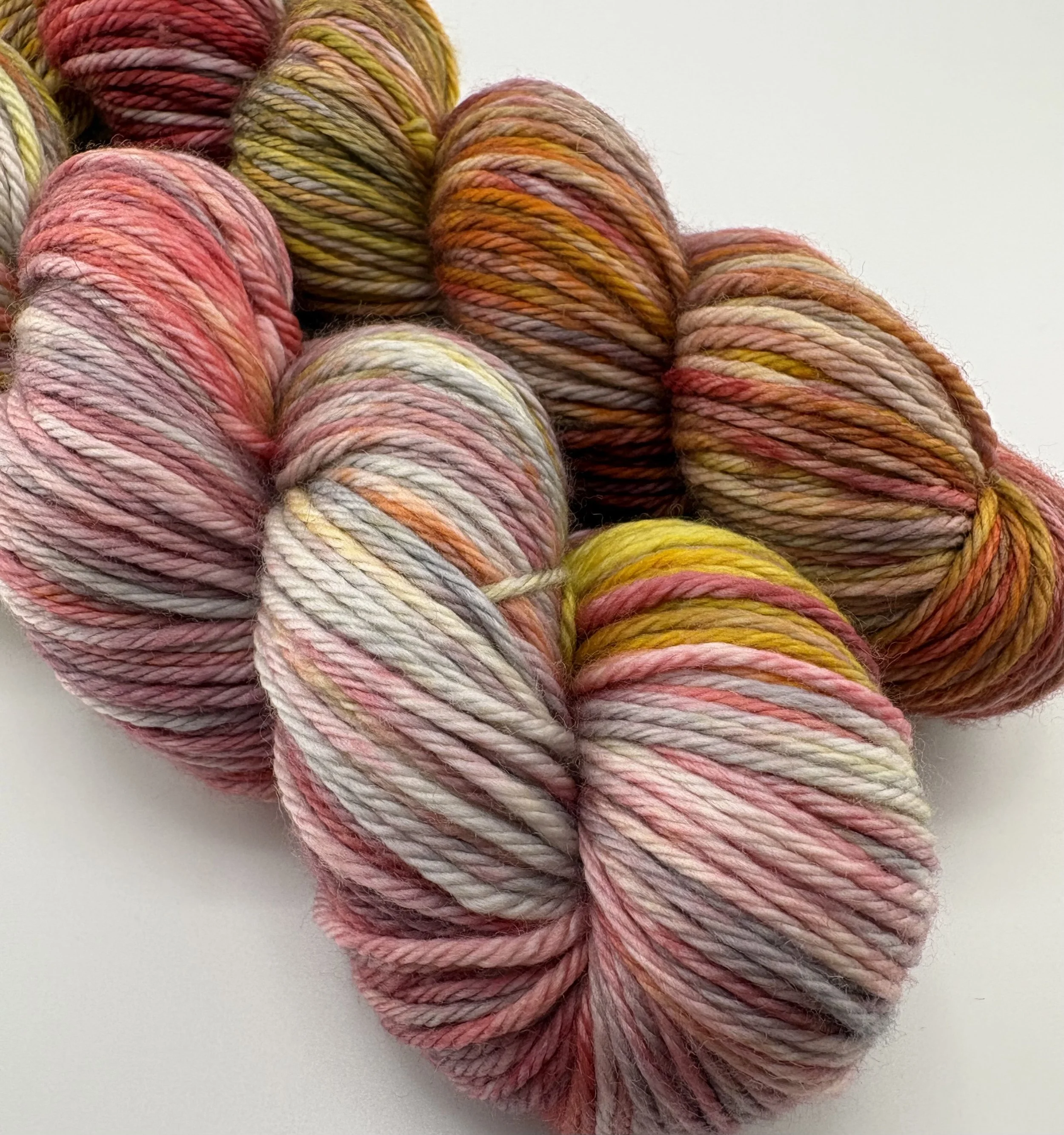 Hand‑dyed yarn skeins in pink, grey, yellow and brown variegated shades