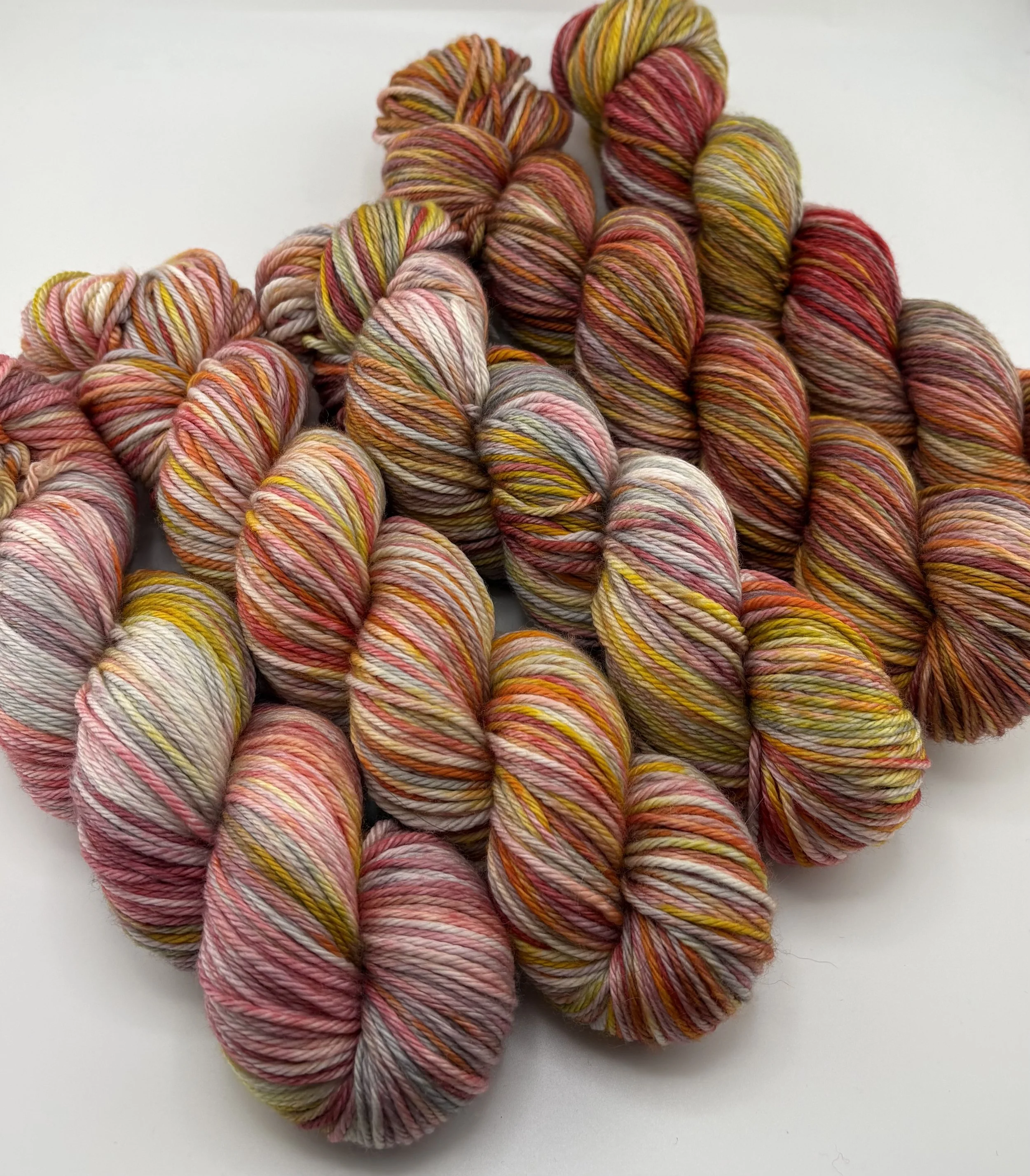 Hand‑dyed yarn skeins in red, pink, yellow, orange and grey variegated shades arranged together
