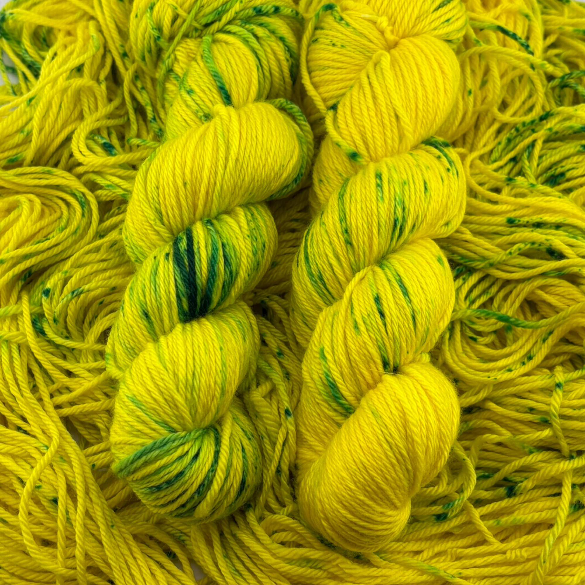 Hand‑dyed yellow‑green yarn skeins displayed on layered loose fibres, showing contrast between smooth twisted skeins and textured strands