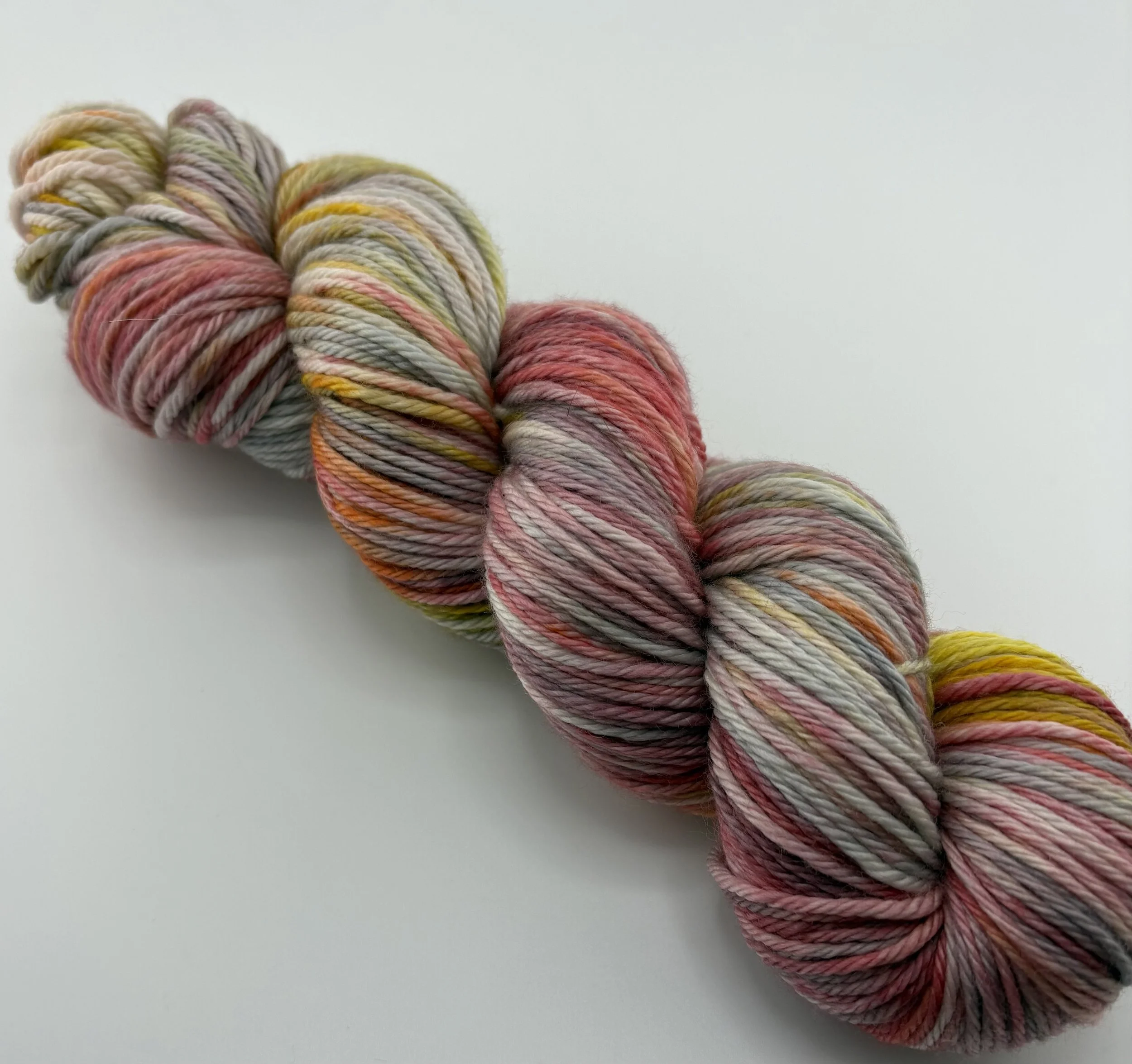 A close up of a Hand‑dyed yarn skein in pink, grey, yellow and brown variegated shades
