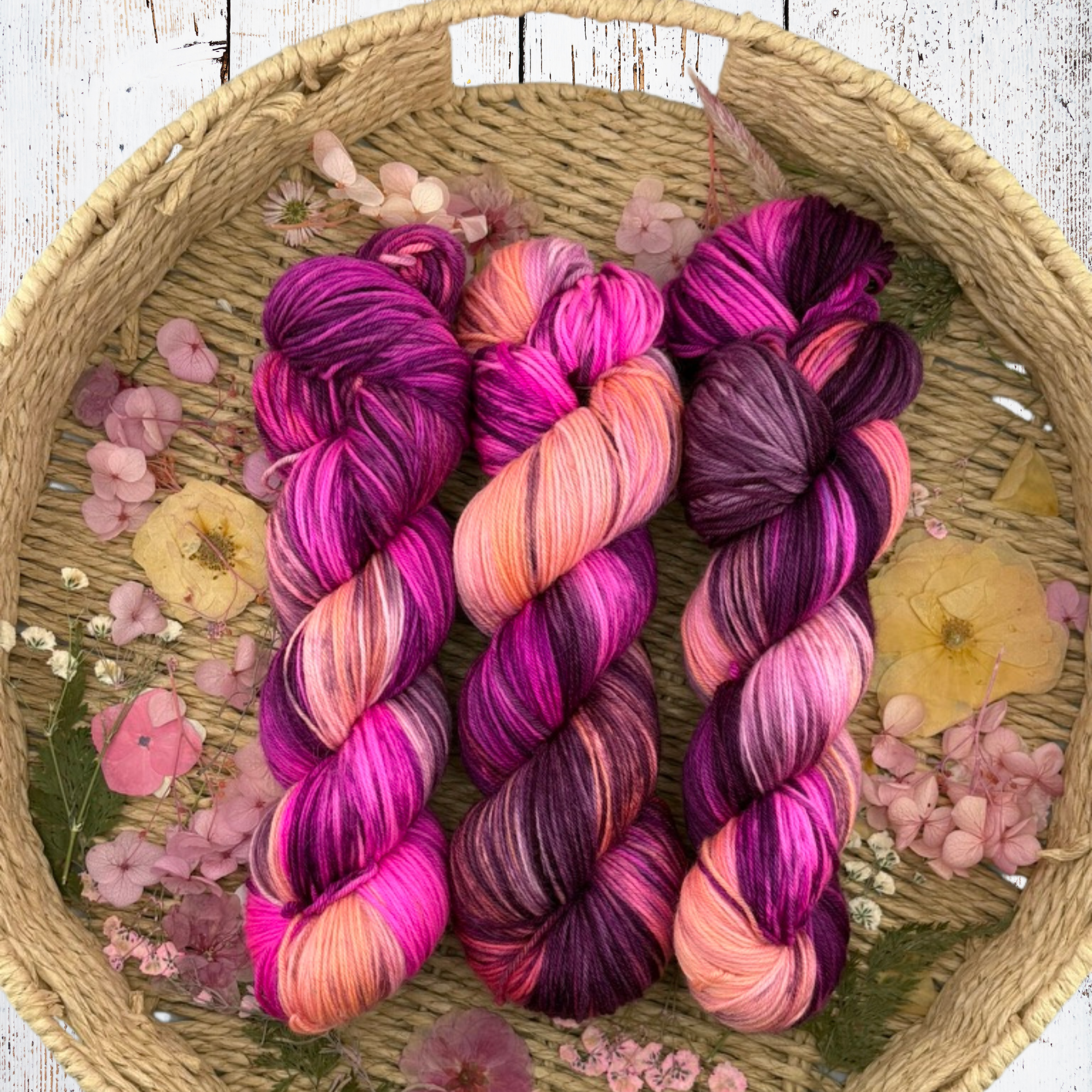 Group of pastel‑to‑vibrant pink and purple yarn skeins arranged neatly to show colour depth and fibre texture