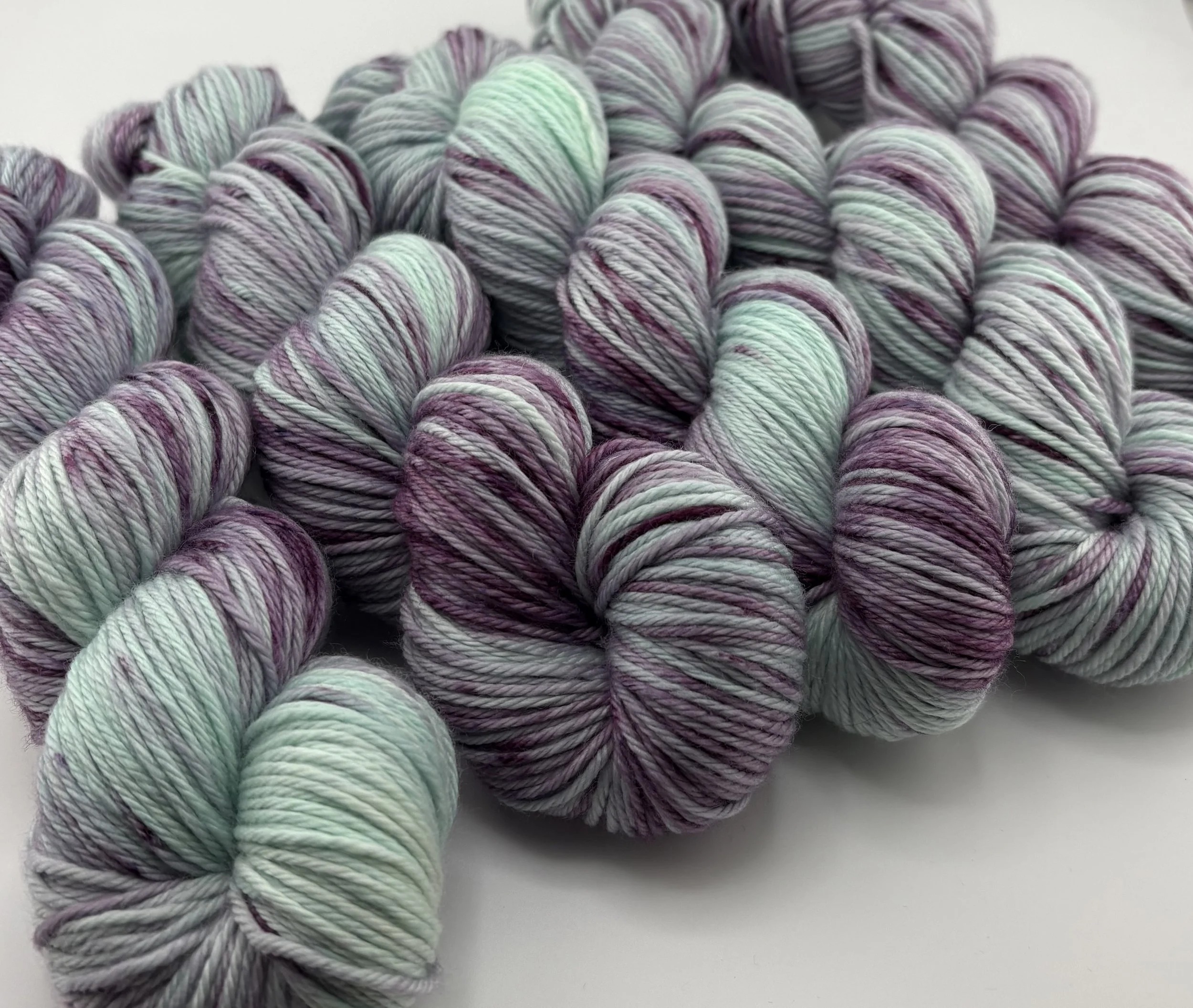 Hand‑dyed yarn skeins in mint green and deep purple variegated shades arranged together