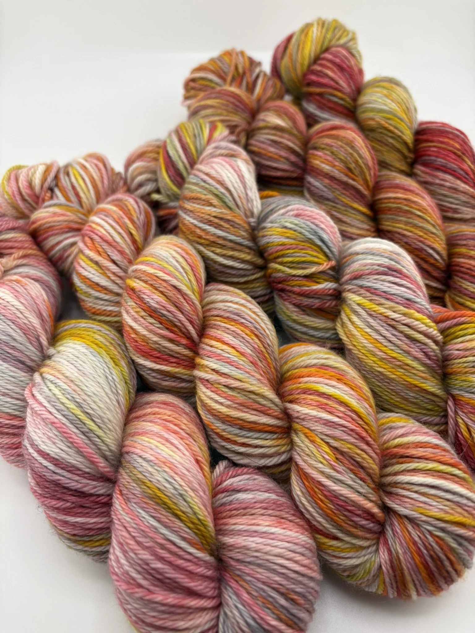 Hand‑dyed yarn skeins in red, pink, yellow, orange and grey variegated shades arranged together