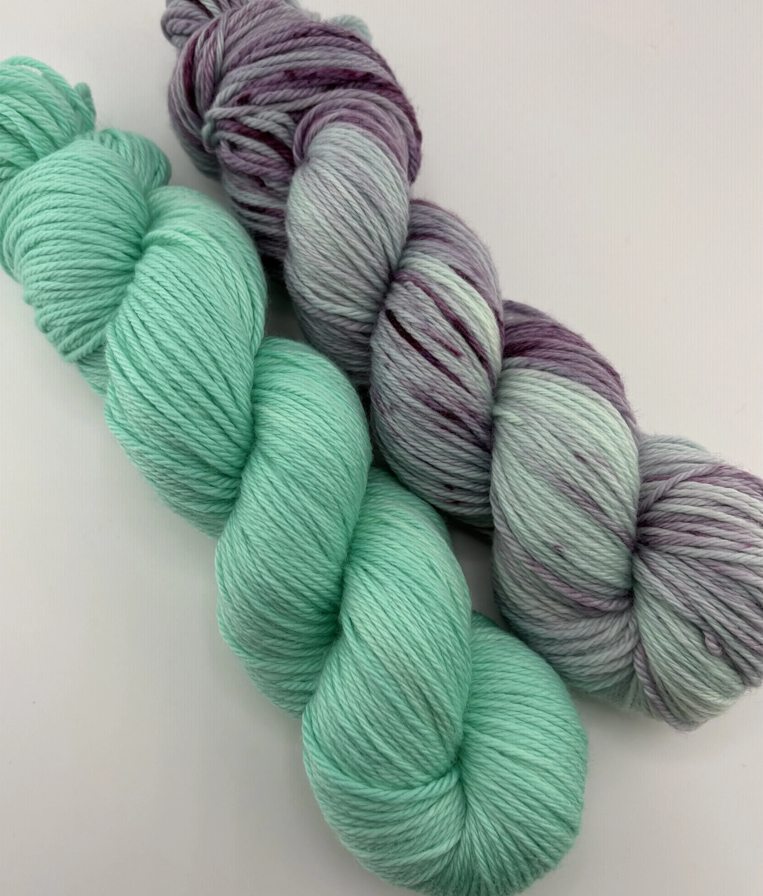 A close up of two skeins of hand dyed yarn - one mint colour and one with teal and purple