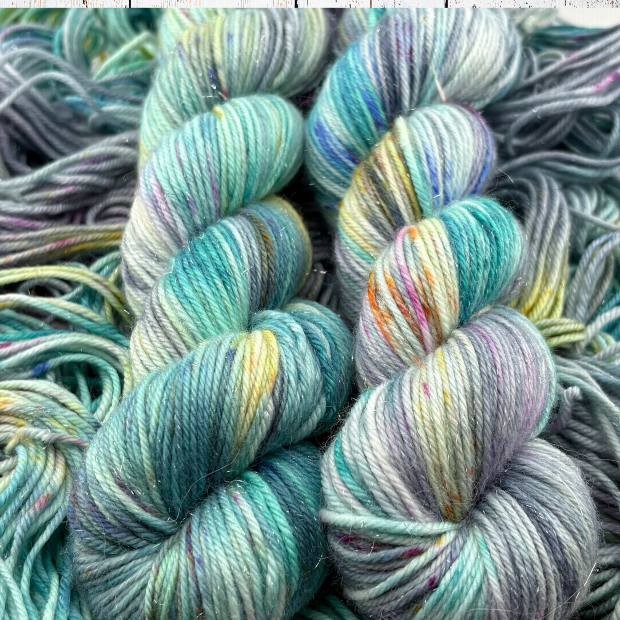 Soft teal and turquoise yarn skeins with hints of yellow and pink displayed on a textured background