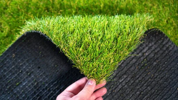 Close-up of a hand holding a patch of green grass with a black textured mat underneath.