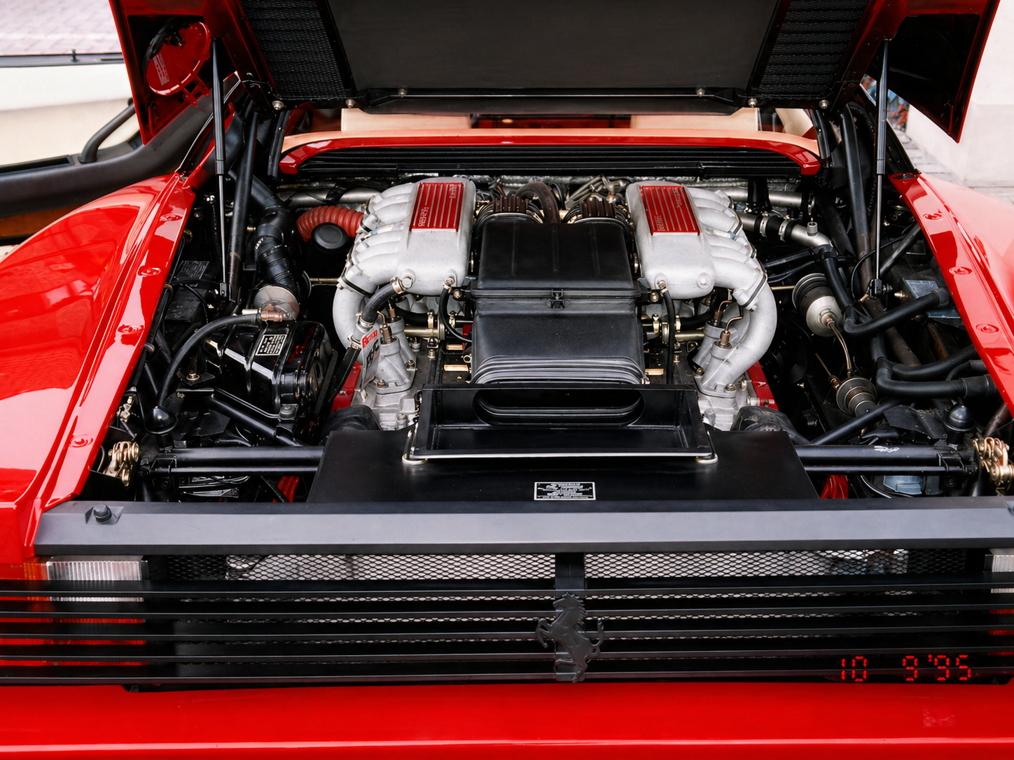 Close-up of a Ferrari Testarossa engine in a red sports car with detailed components and visible wiring.