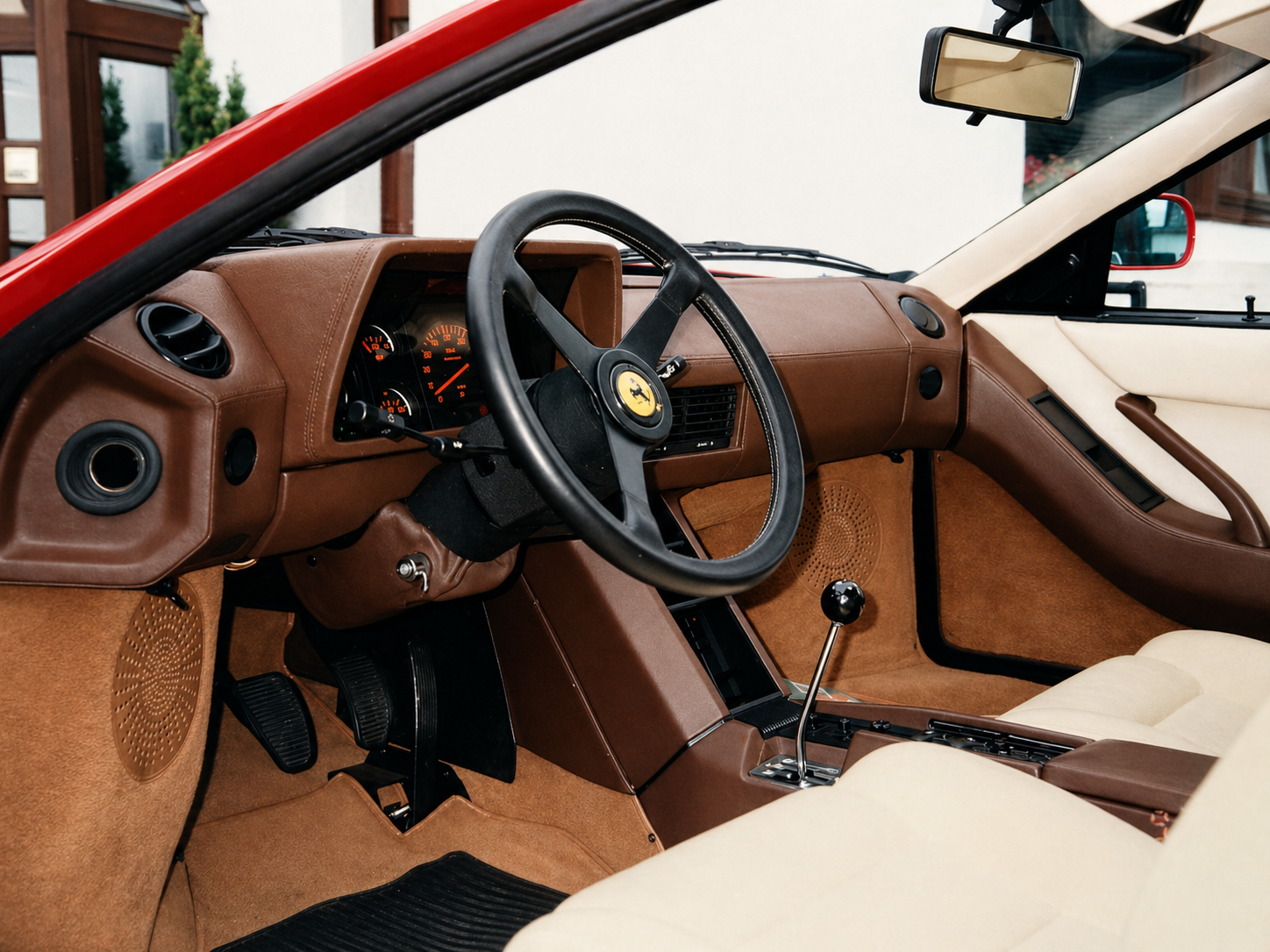 Interior of a vintage Testarossa Ferrari car with brown leather upholstery, a three-spoke steering wheel featuring the Ferrari emblem, and a manual gear shift lever.