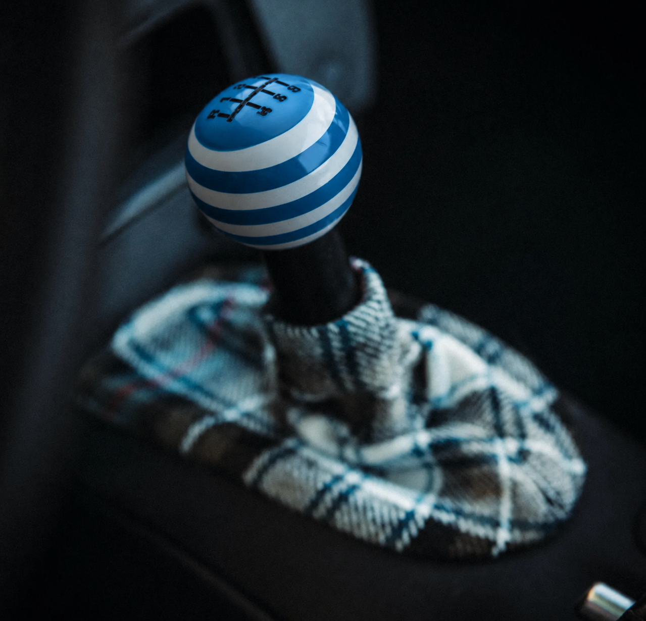 Close-up of a gear shift knob with a blue and white striped ball, situated in a car's interior, with a plaid cloth nearby.