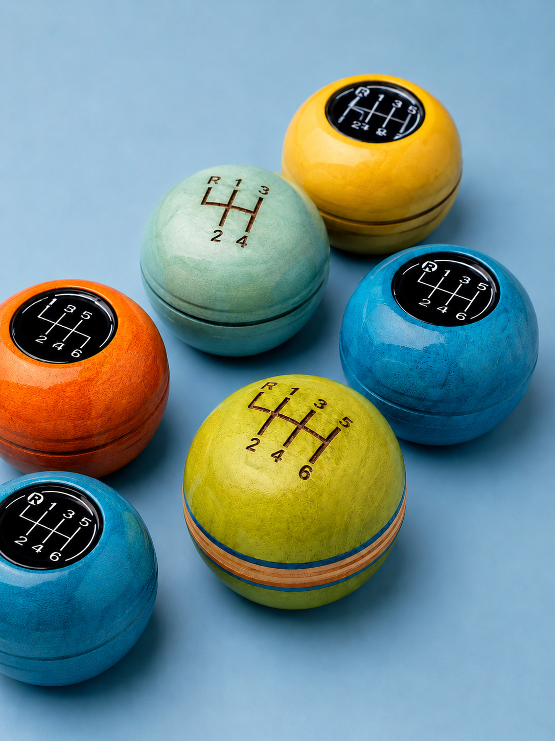 Colorful tennis ball-shaped gear shift knobs for cars, each with a different gear pattern, placed on a light blue background.