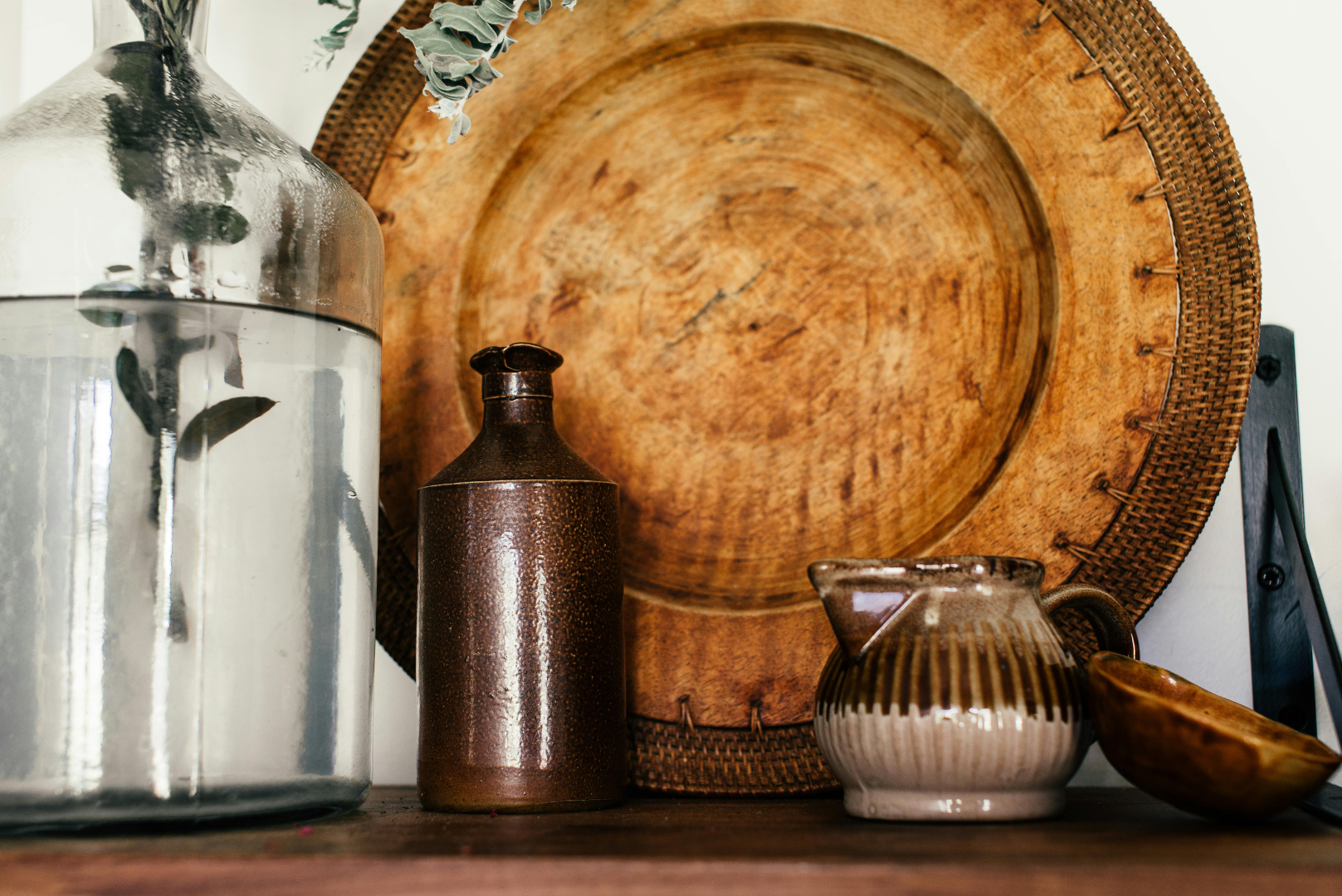 Decorative rustic vases and bowls on a wooden surface in front of a large round wooden tray.