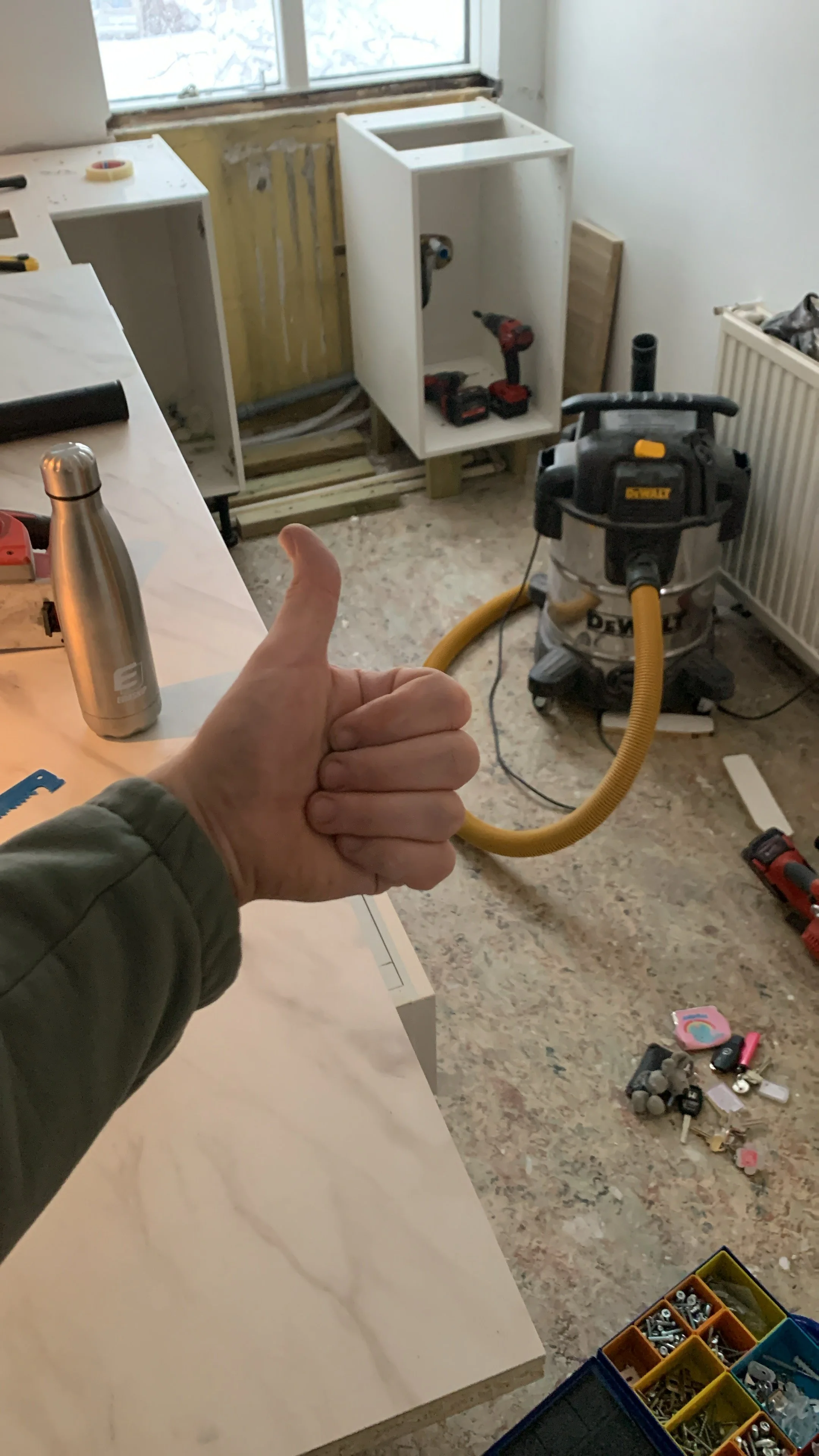 Thumbs up in front of a kitchen renovation scene with a marble countertop, a construction vacuum, tools, and building materials.