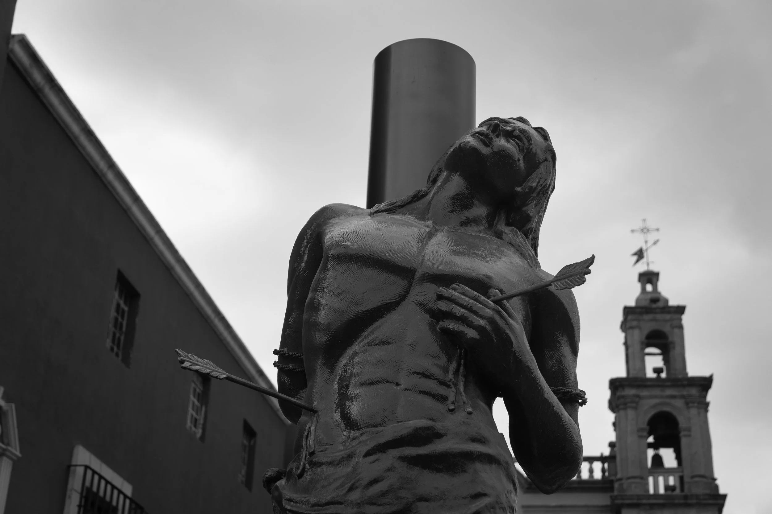 Una escultura de hombre flechado con un fondo de campanario, en blanco y negro. (c) 2026 Héctor Obregón
