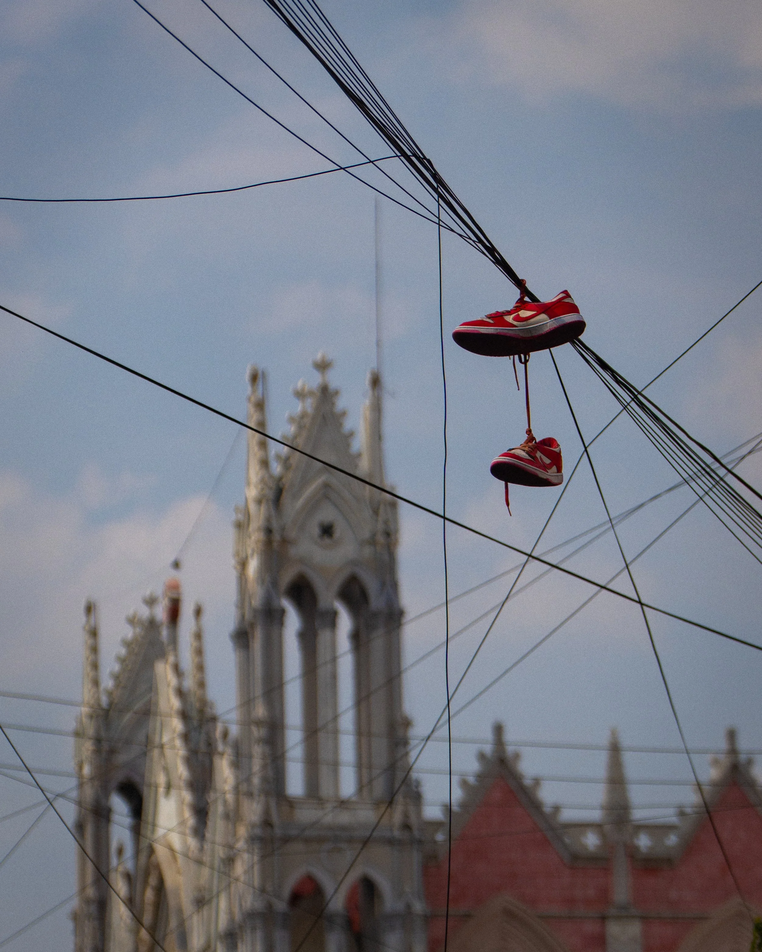 Unos tenis rojos colgados de cables eléctricos con una iglesia de fondo. (c) 2026 Héctor Obregón
