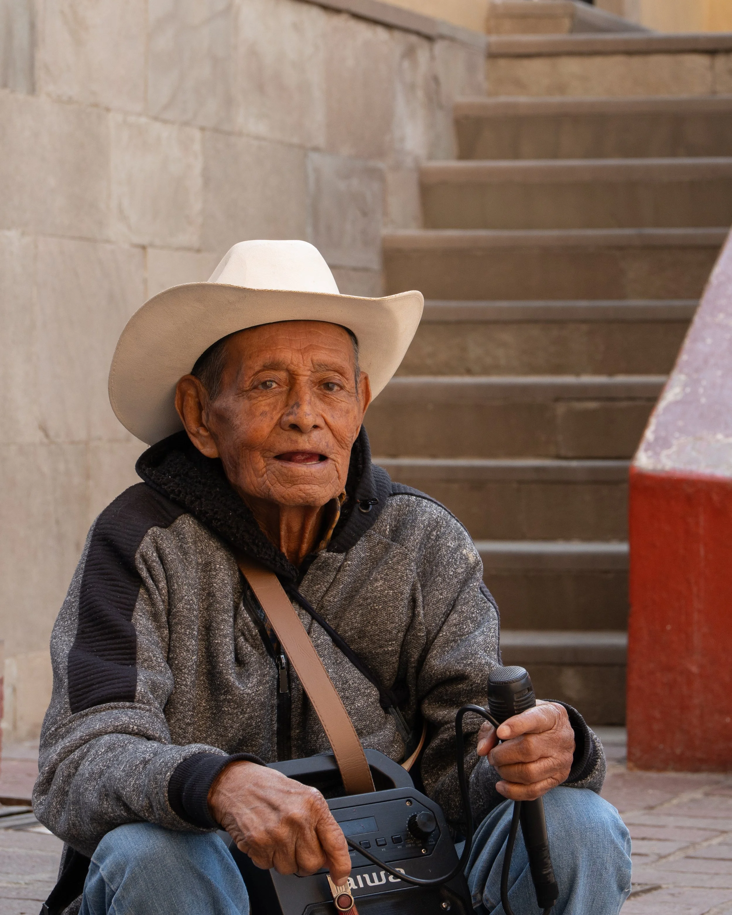 Un hombre de la tercera edad con un micrófono al pie de una escalinata. (c) 2025 Héctor Obregón