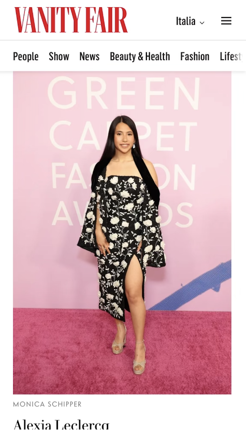 A woman in a black and white floral dress with a thigh-high slit posing on a pink carpet at the Vanity Fair Green Carpet Fashion Awards event.