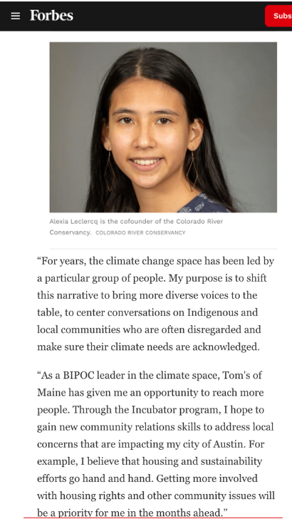 Headshot of a young woman with long dark hair smiling, wearing a dark top with a patterned neckline, against a gray background.