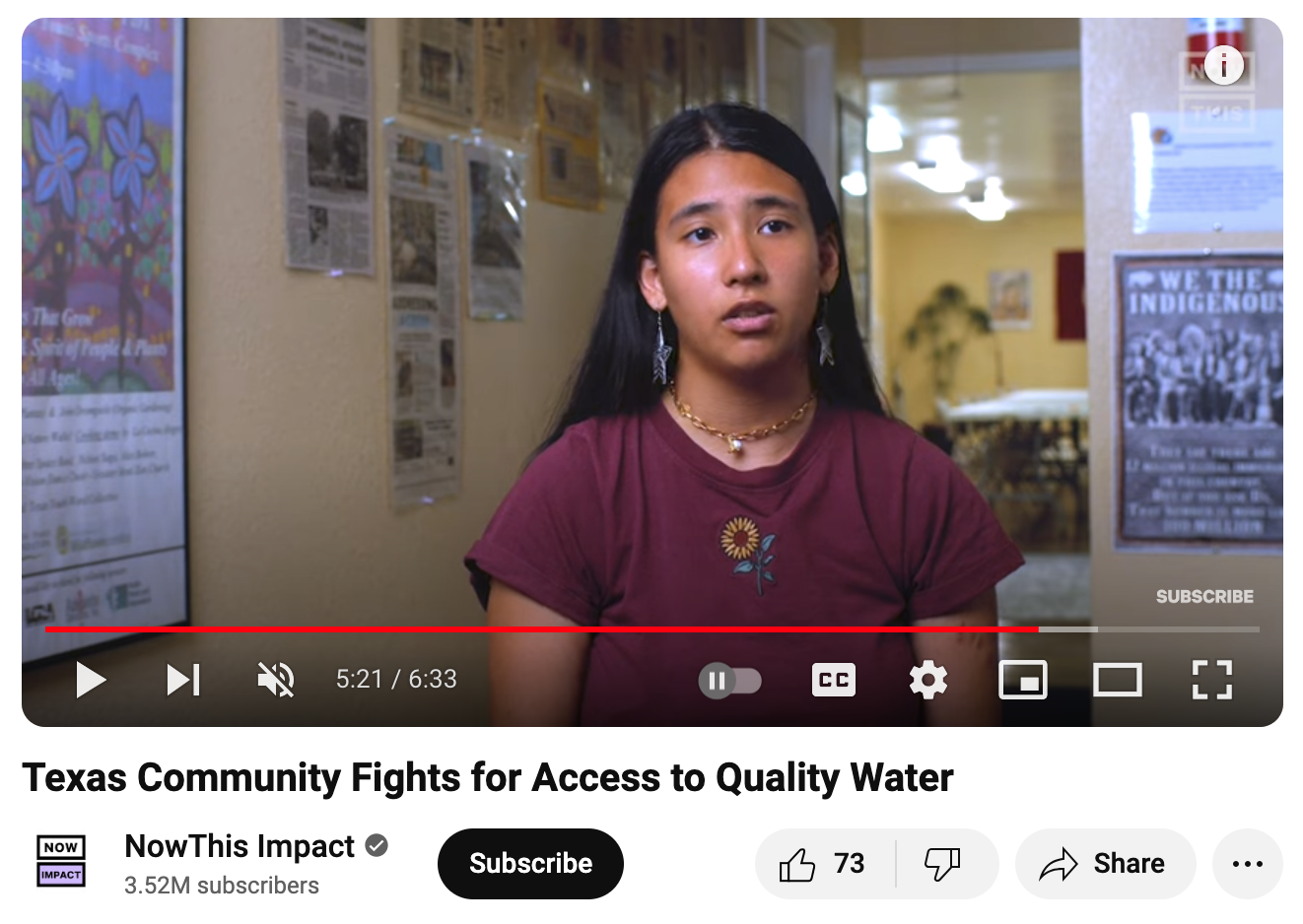 A young woman with long black hair, wearing a maroon shirt with a sunflower embroidery, earrings, and a necklace, speaking in an indoor setting with posters on the wall behind her.
