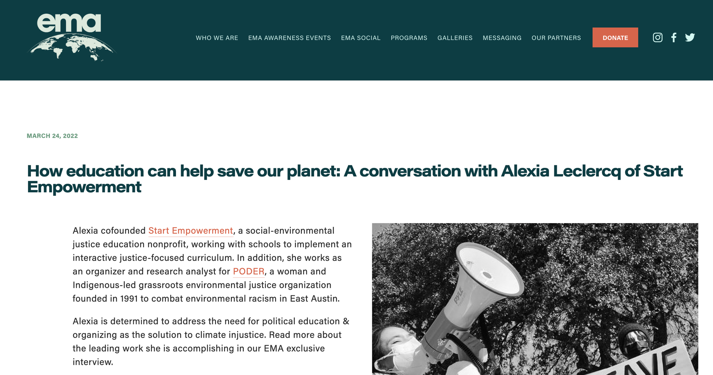 A person holding a megaphone and a microphone at an outdoor protest or rally. The background includes trees and part of a sign.