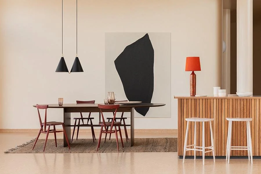 Modern dining area with a black and red color scheme, featuring a wooden table with red chairs, a painting on the wall, and a wooden bar with two white stools and a red lamp.