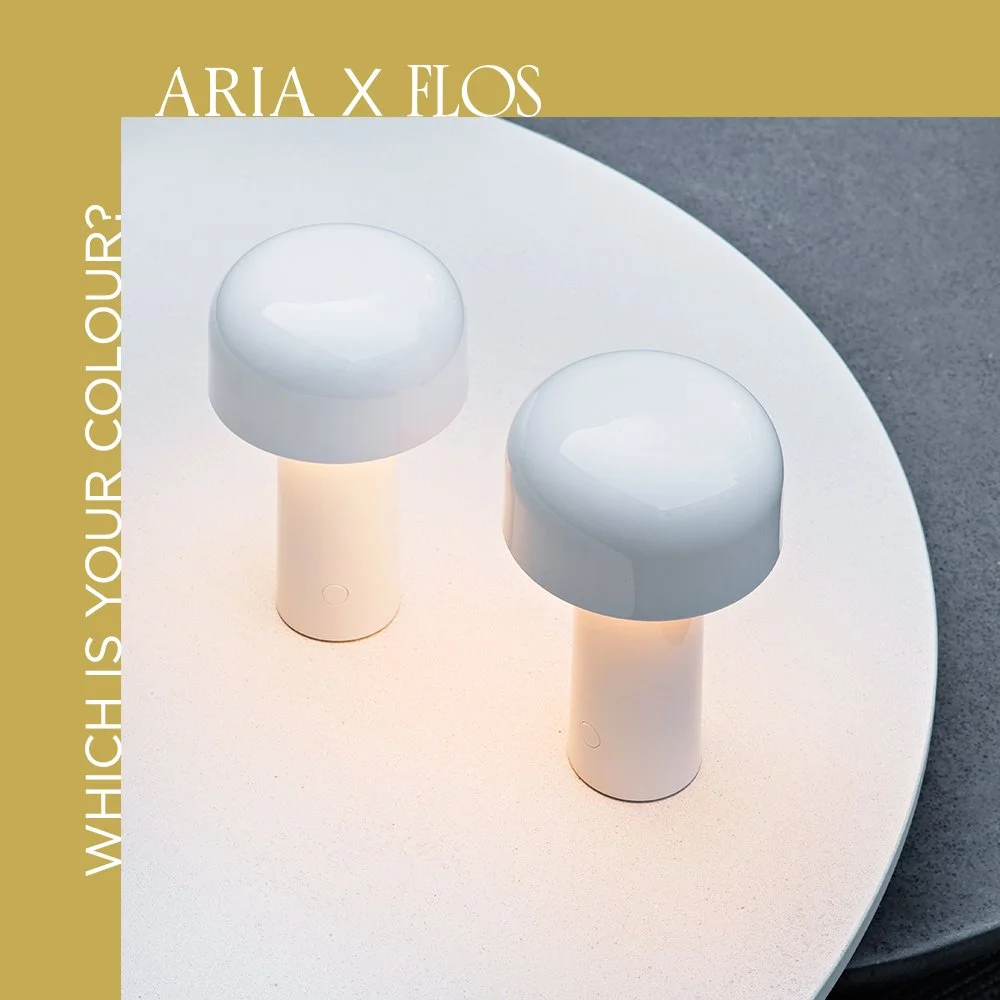 Two modern, white, mushroom-shaped table lamps with rounded tops and cylindrical bases on a white round table, against a gray and dark background.