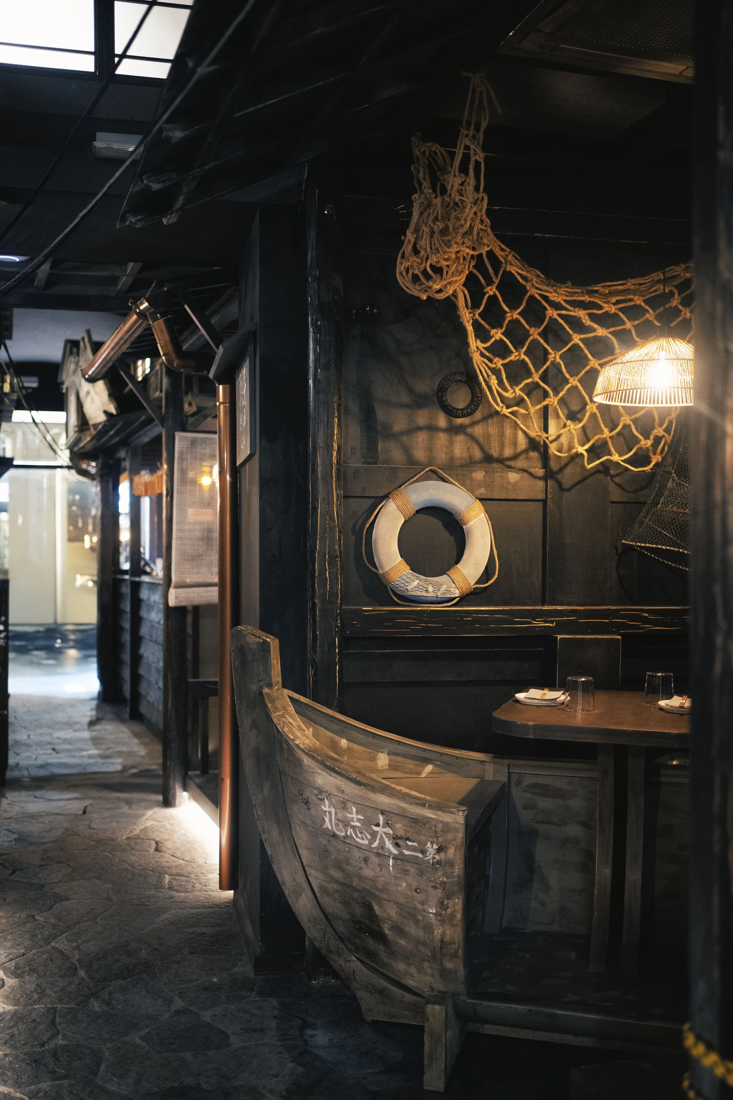 Decorazioni a tema marino con rete e salvagente in un ambiente di ristorante o bar, con tavoli apparecchiati e illuminazione calda.