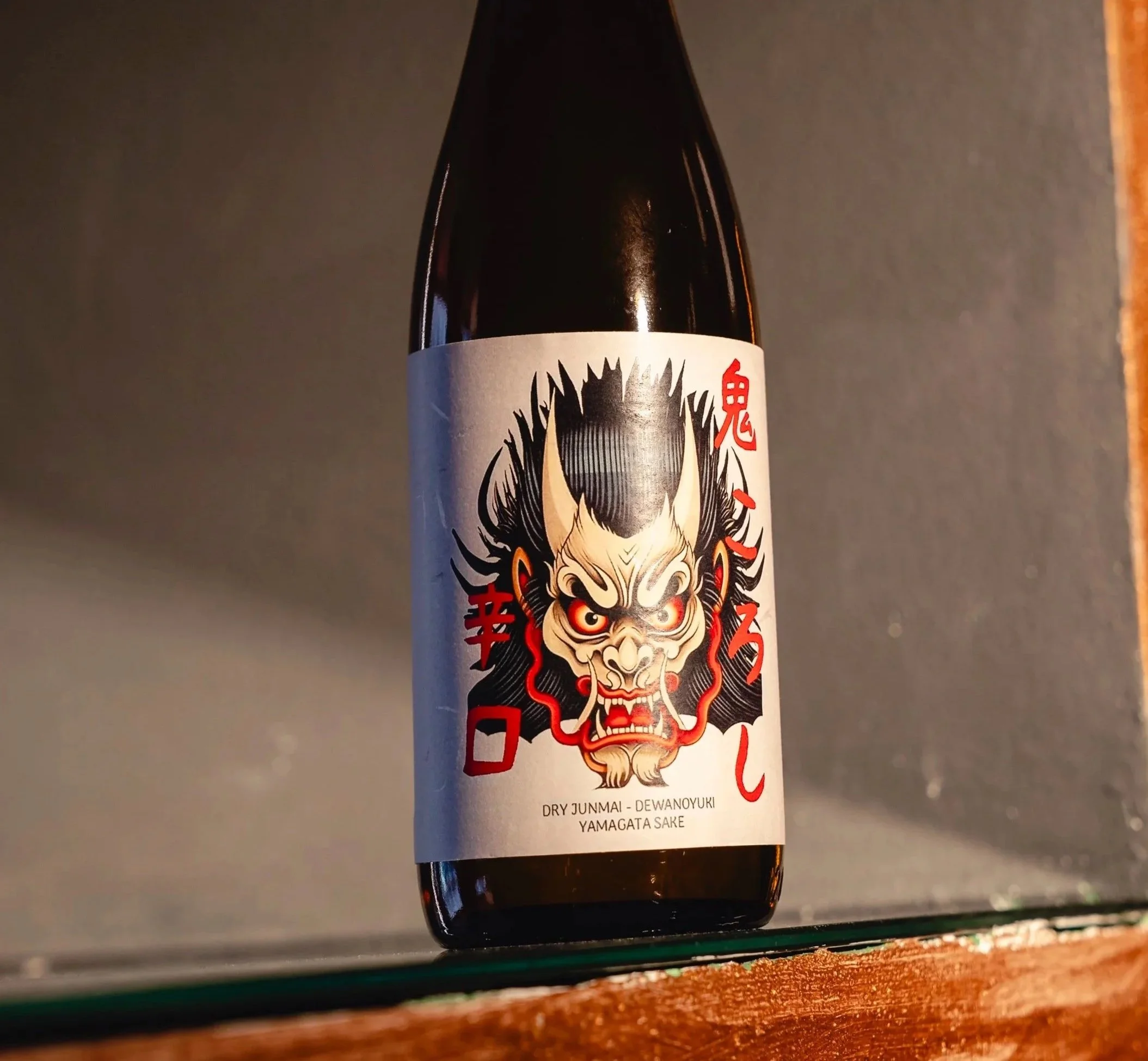 Bottiglia di saké con etichetta artistica raffigurante un demone con tratti sfumati e testo in giapponese e inglese.