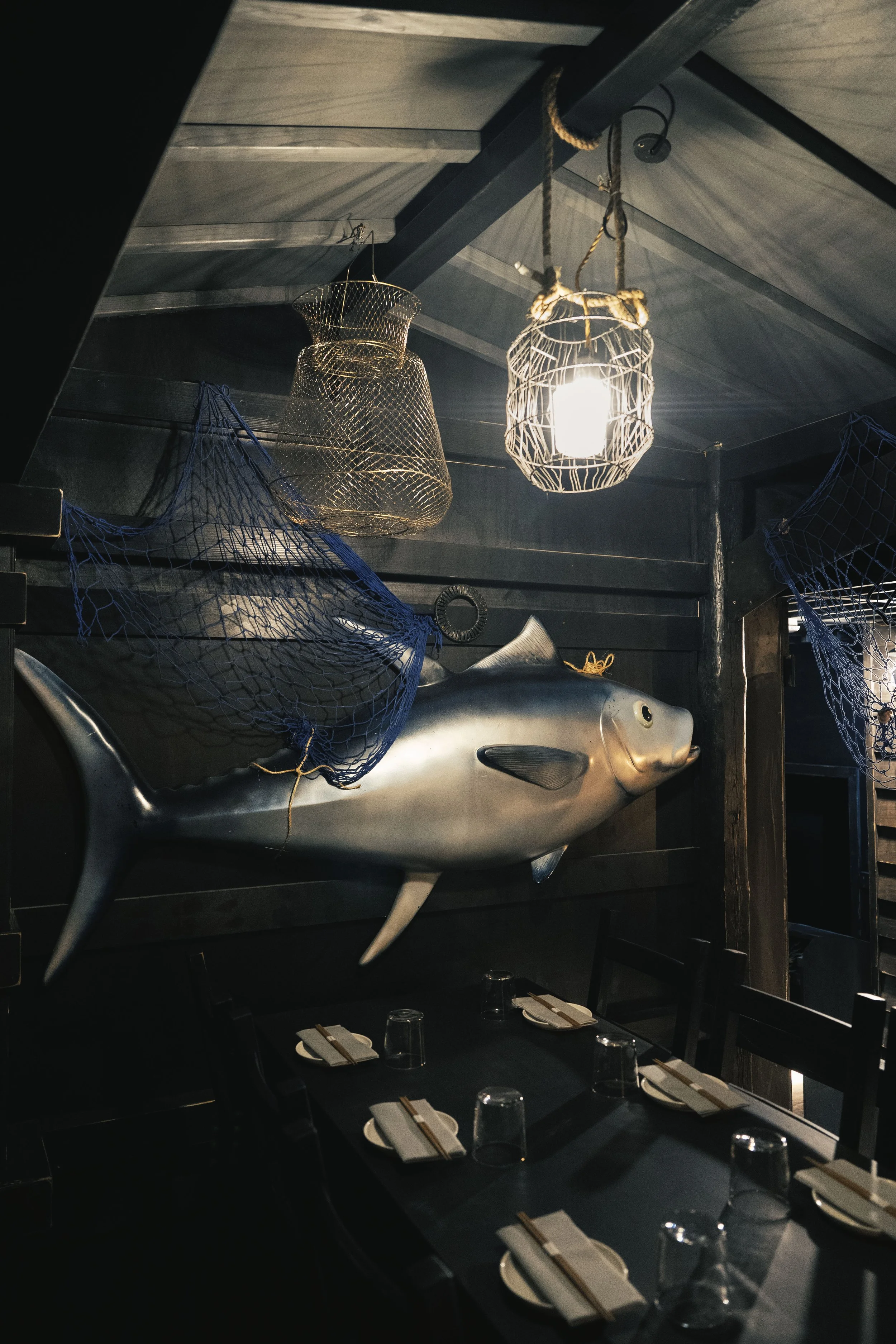 Interno di un ristorante con decorazione a tema marittimo, include un grosso pesce metallico appeso al muro e lanterne sospese nel soffitto.