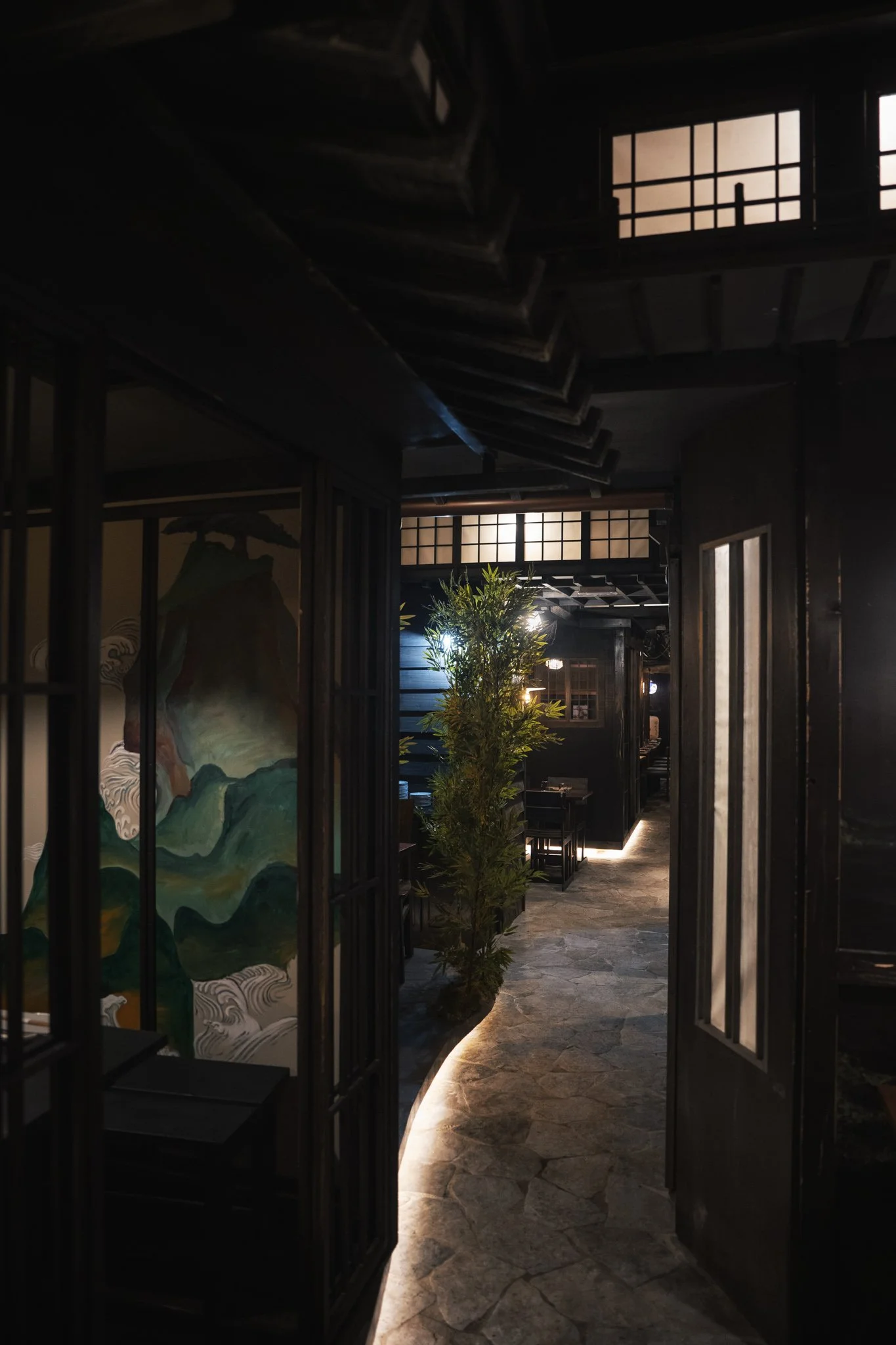 Interno di un ristorante con pareti nere, illuminazione soffusa, piante e dettagli in stile giapponese.