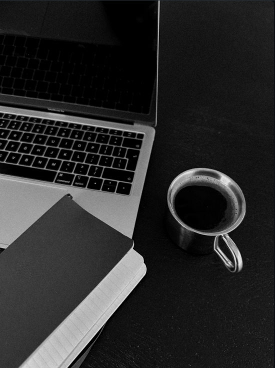 Open laptop, closed planner, and a coffee mug on a dark surface.