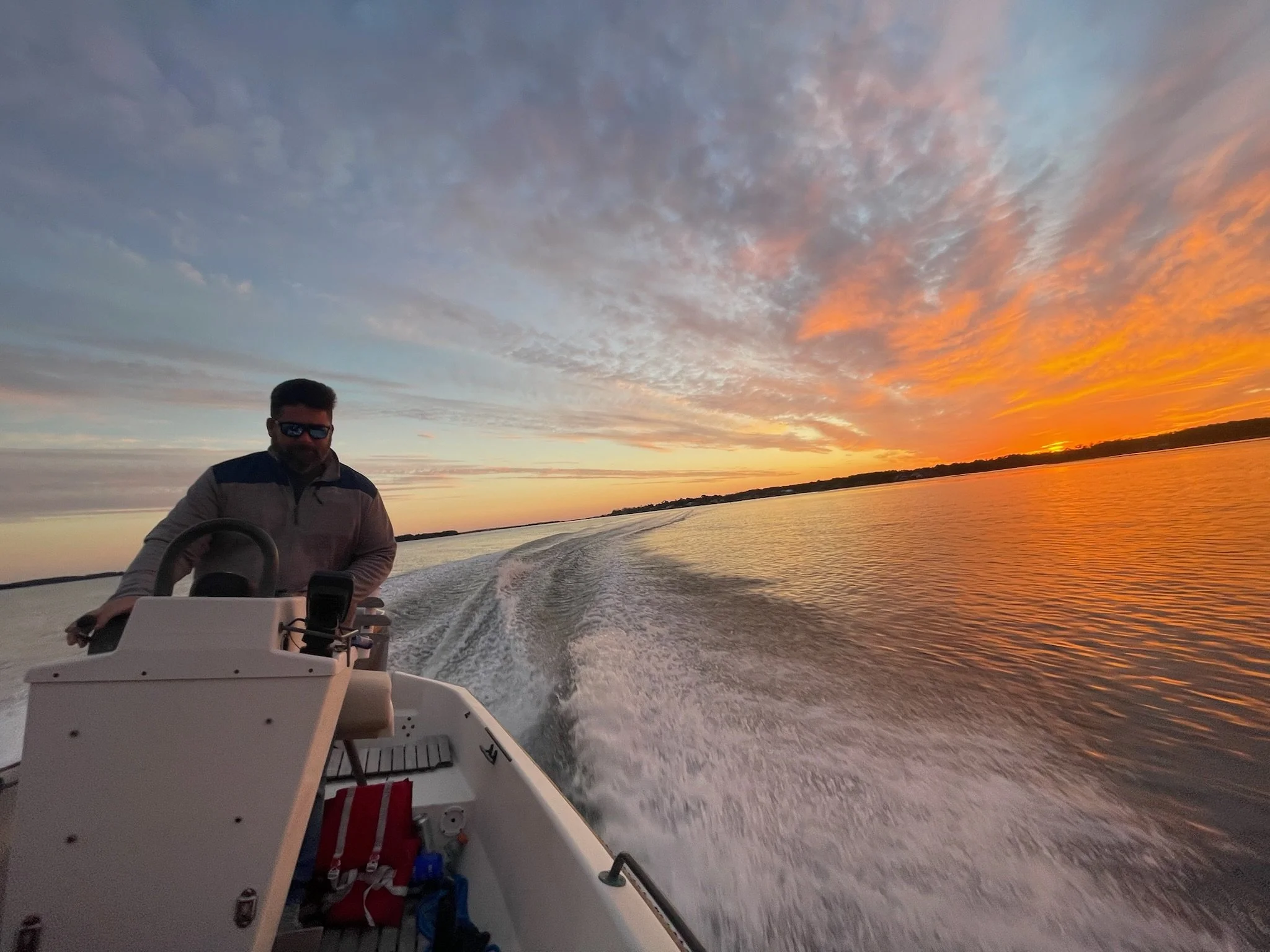 Captain Seth Daniel during a sunset tour on White Oak River steering a boat on a river at sunset, with colorful clouds and orange sky in the background.