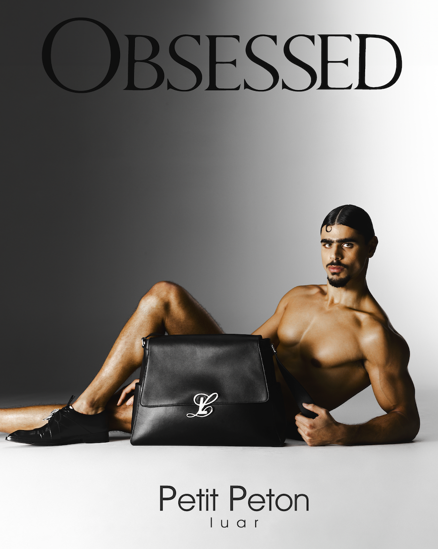A shirtless man with dark hair and a mustache lying on the floor, holding a black handbag with the initials "LB" in front of a gray background. The words "OBSESSED" are at the top and "Petit Peton l u a r" are at the bottom.