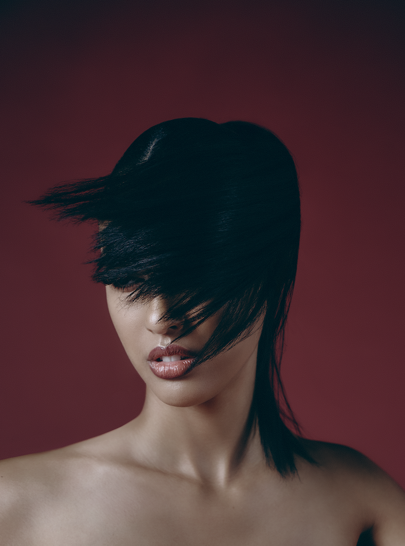 A woman with black hair covering her eyes against a red background.