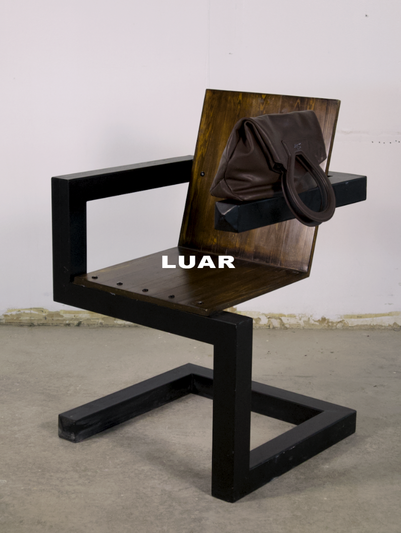 A modern black and wood chair with a brown handbag hanging on the backrest. The word "LUAR" is written in white text on the seat of the chair.