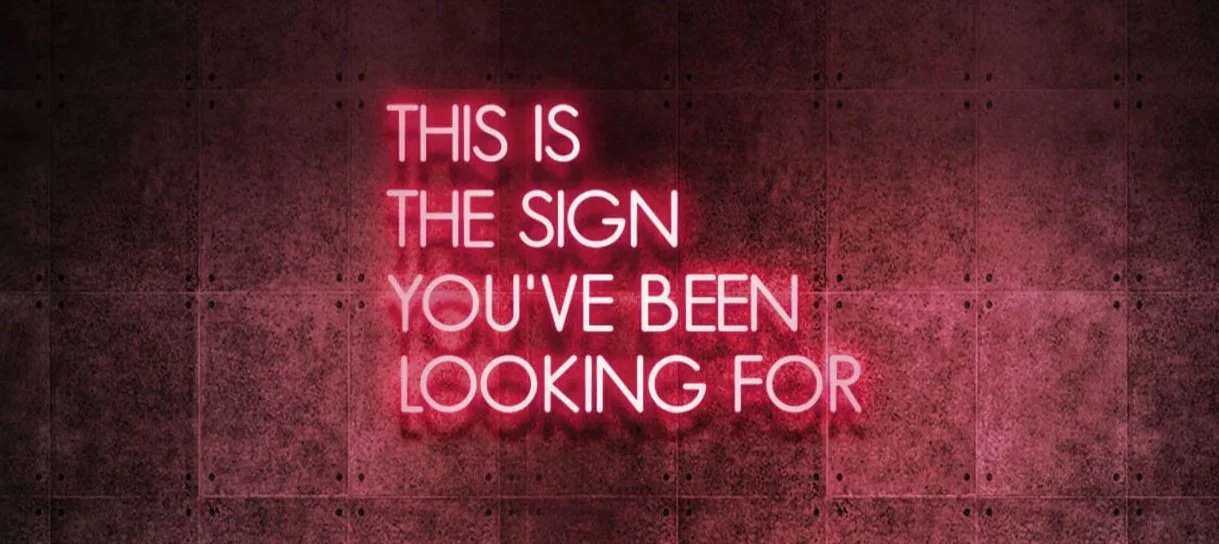 Pink neon sign on a dark wall that reads, "This is the sign you've been looking for."